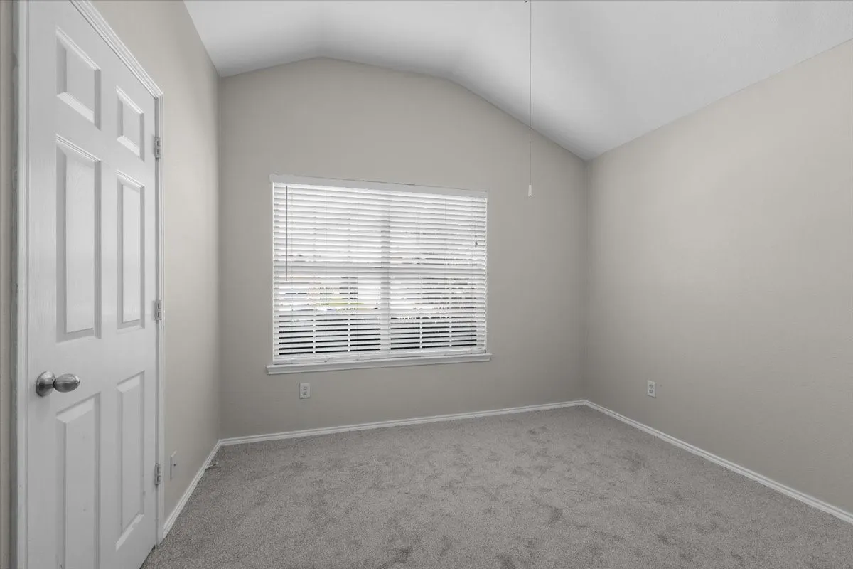 Vaulted ceiling with a window and horizontal blinds, neutral wall paint, and gray carpet