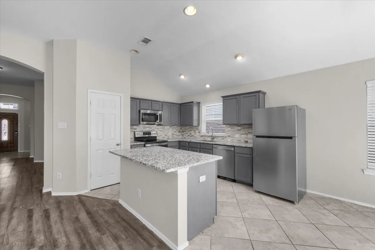 Kitchen with vaulted ceiling, recessed lighting, stainless steel appliances, grey cabinetry, and a central island with a stone-finish countertop