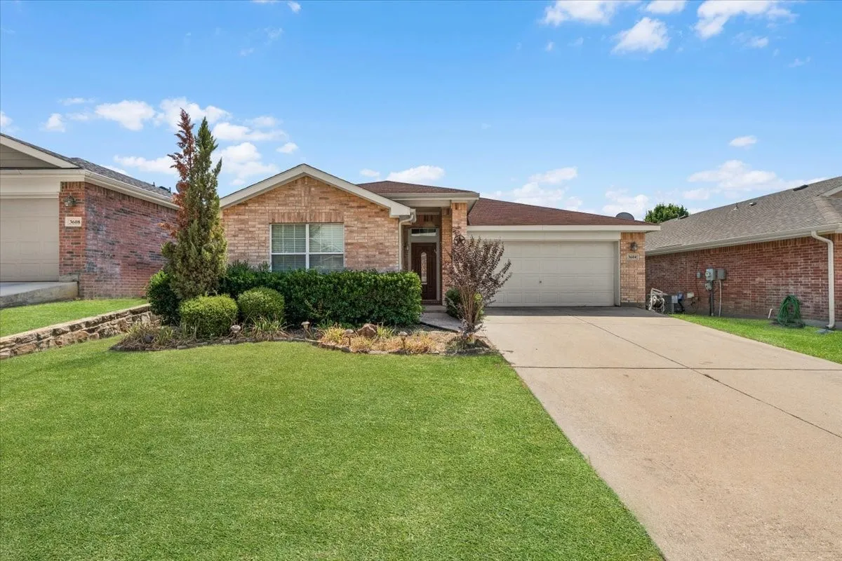 Brick exterior with an attached garage, concrete driveway, and front landscaping