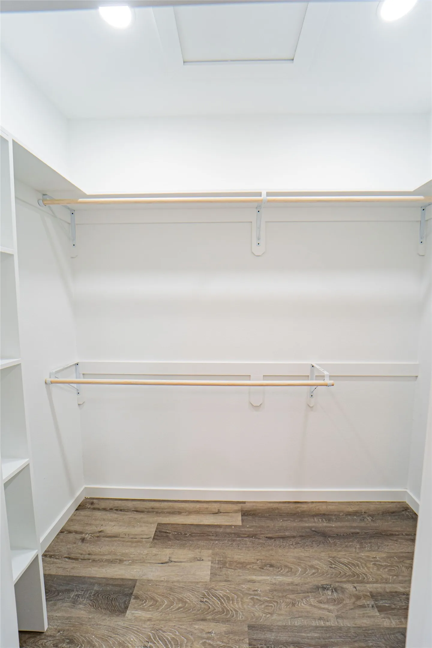 White walls with recessed lighting, wood-finish flooring, two wooden rods for hanging, and integrated shelving