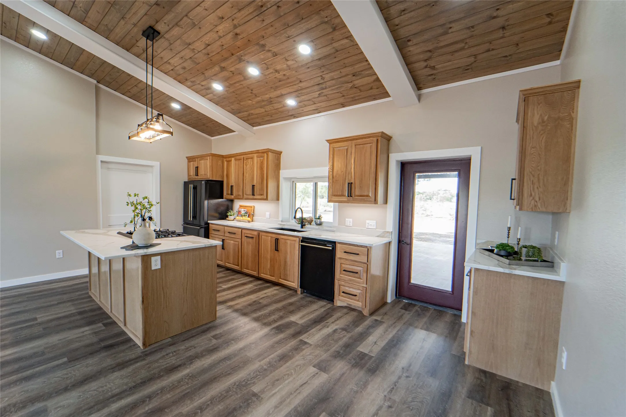 Vaulted wood-finish ceiling with exposed beams, wood-finish flooring, light wood-tone cabinetry, white countertops, and a central island
