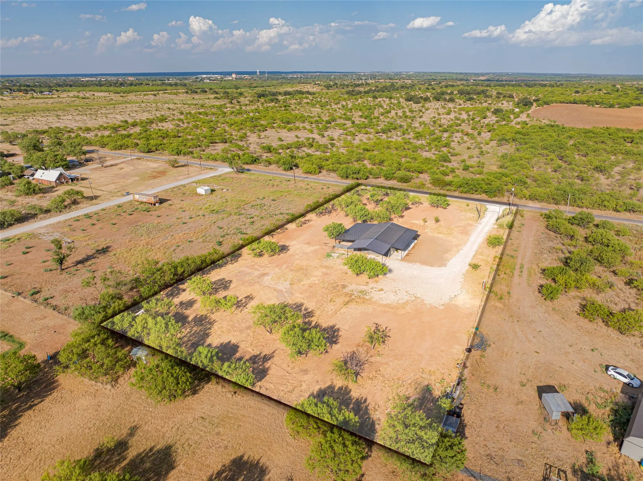 Expansive lot featuring a single-story residence with a dark roof, gravel driveway, and mature trees