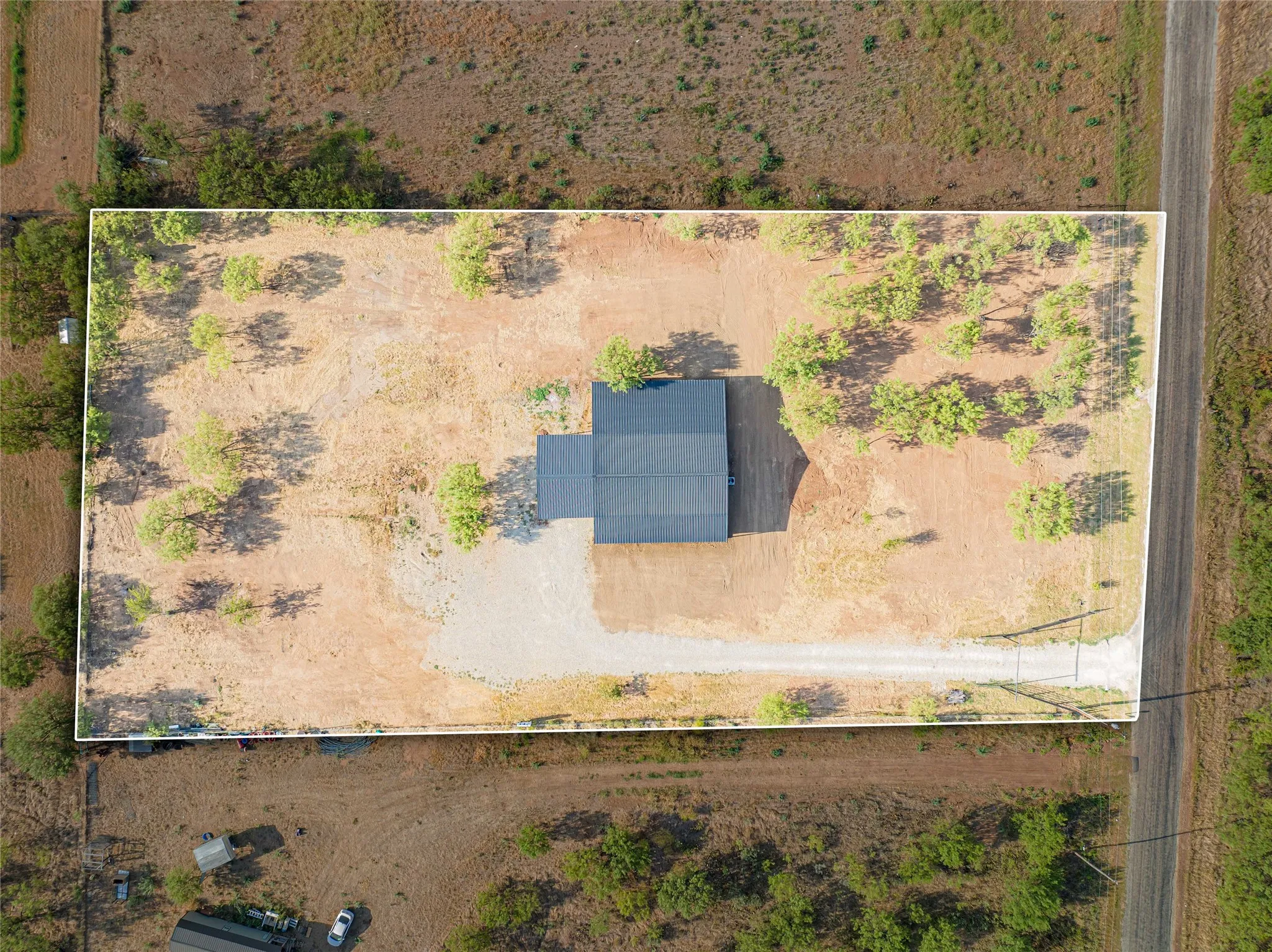 Expansive lot with a detached structure, gravel driveway, and surrounding natural landscaping