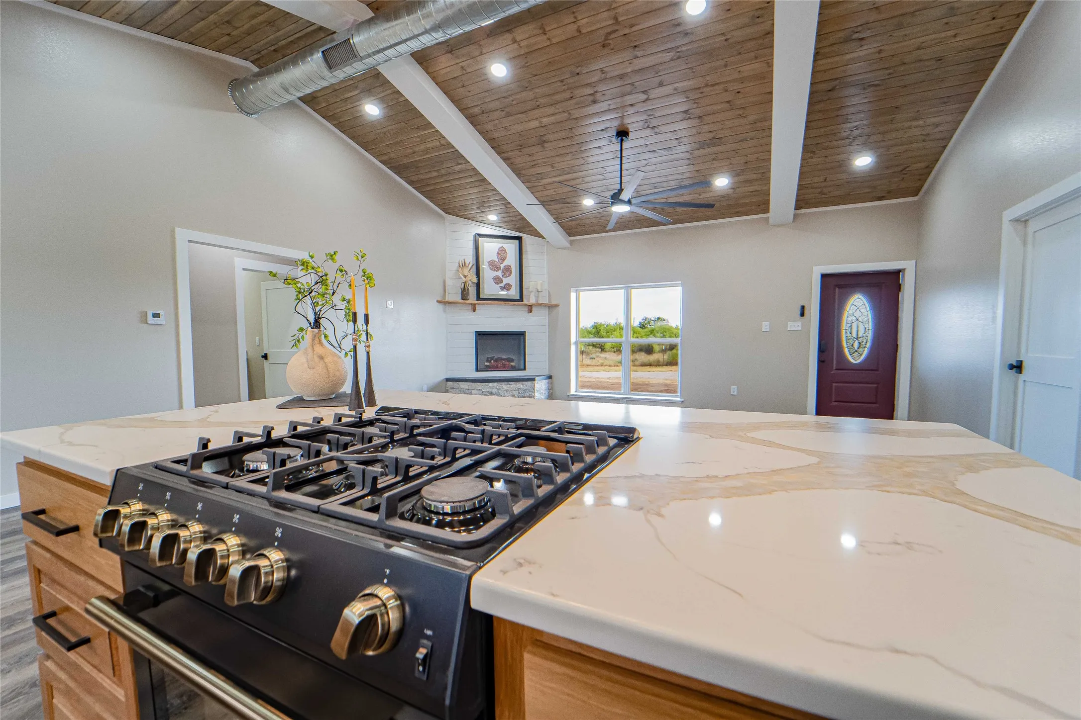 Integrated gas range with gold-tone hardware, a vaulted wood-plank ceiling with exposed beams, recessed lighting, a ceiling fan, and a fireplace with a mantel
