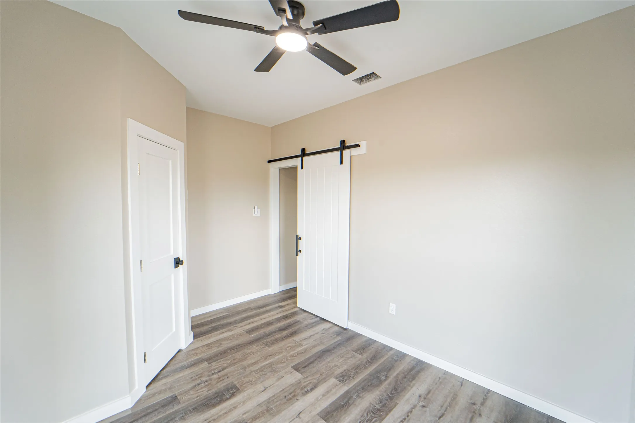 Wood-finish flooring, neutral wall tones, modern ceiling fan, white paneled door, and white barn door