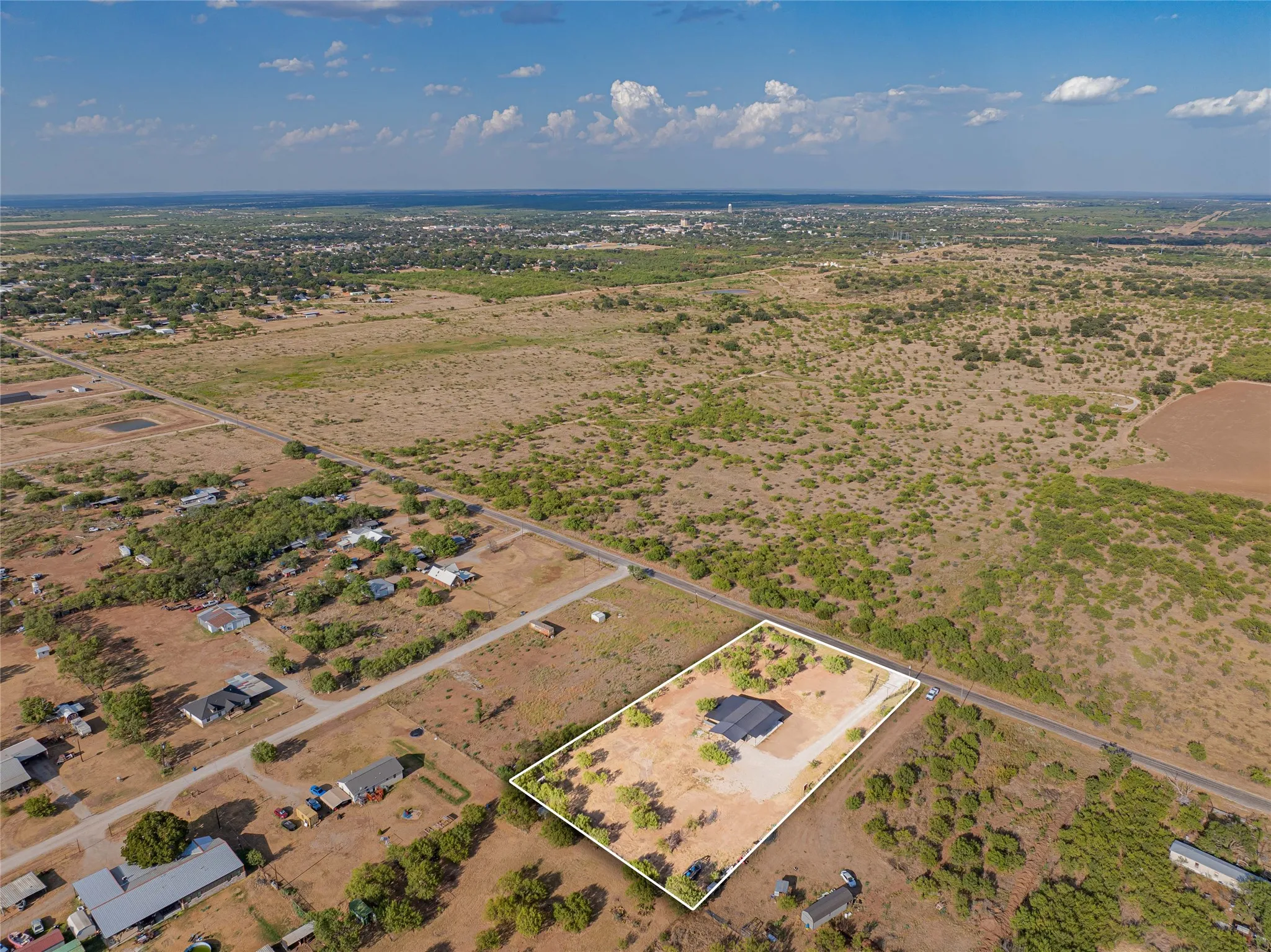 Expansive rural property featuring a single-story residence, surrounding acreage, and a distant town backdrop
