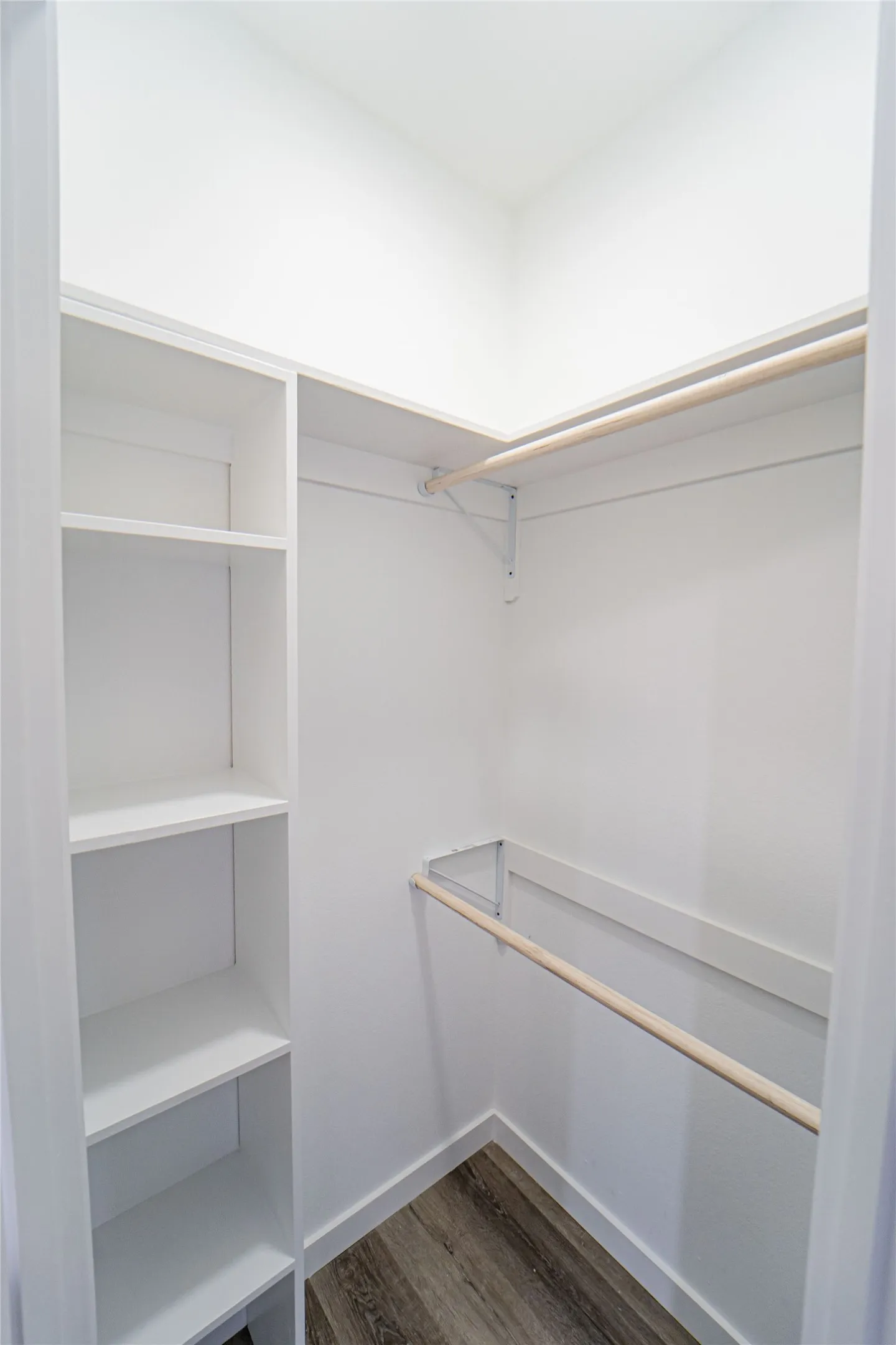 Walk-in closet featuring built-in shelving, dual hanging rods, and wood-finish flooring