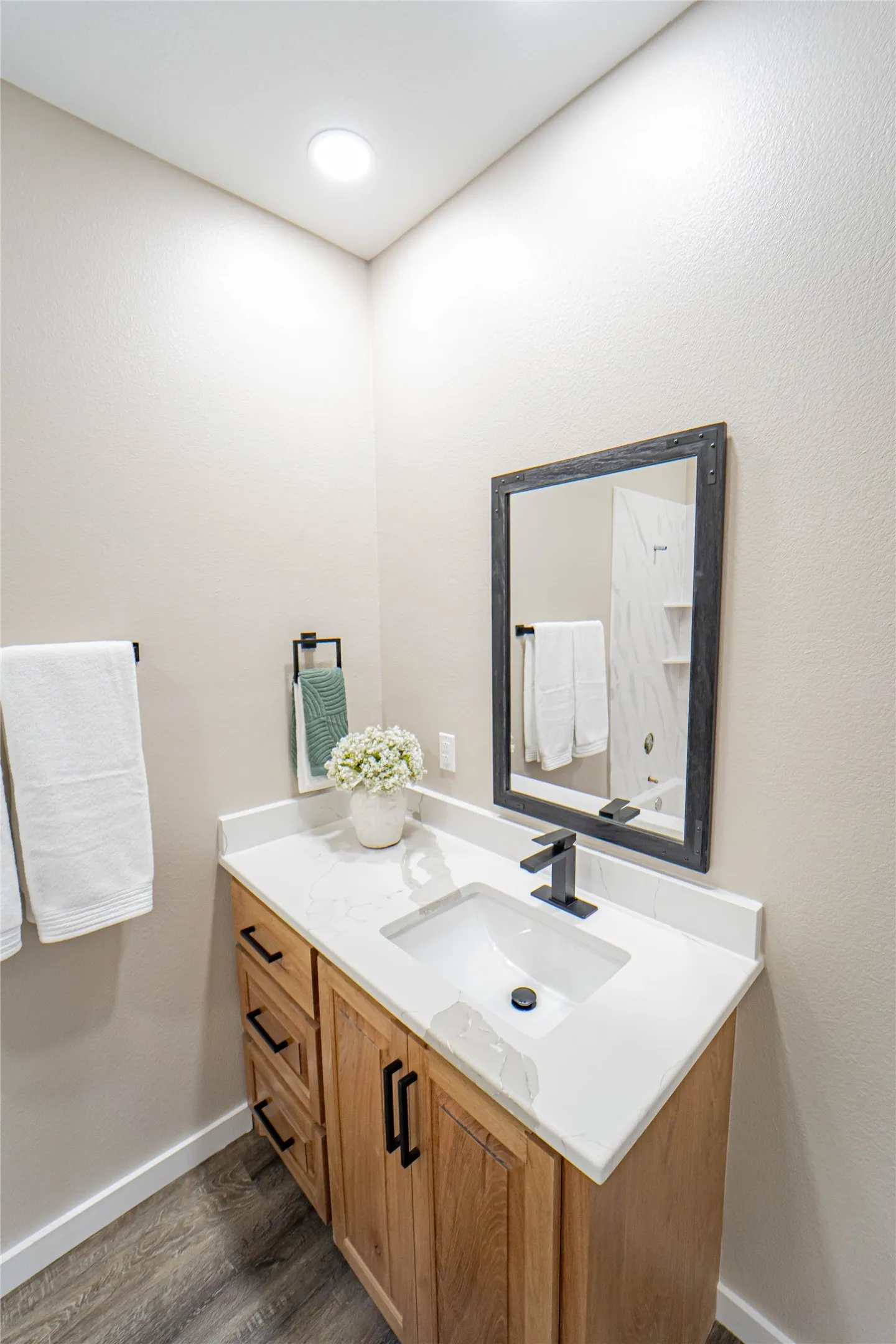 Wood-finish flooring, light wood vanity with matte black hardware, white countertop, and an undermount sink with a matte black faucet