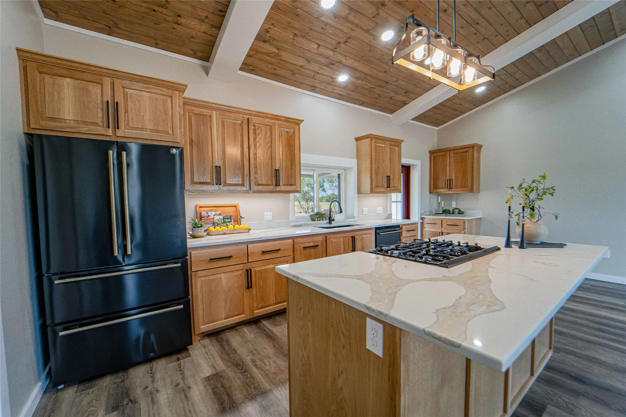 Vaulted ceiling with wood-finish planks, recessed lighting, wood-finish cabinetry, patterned stone countertop island with cooktop, and wood-finish flooring