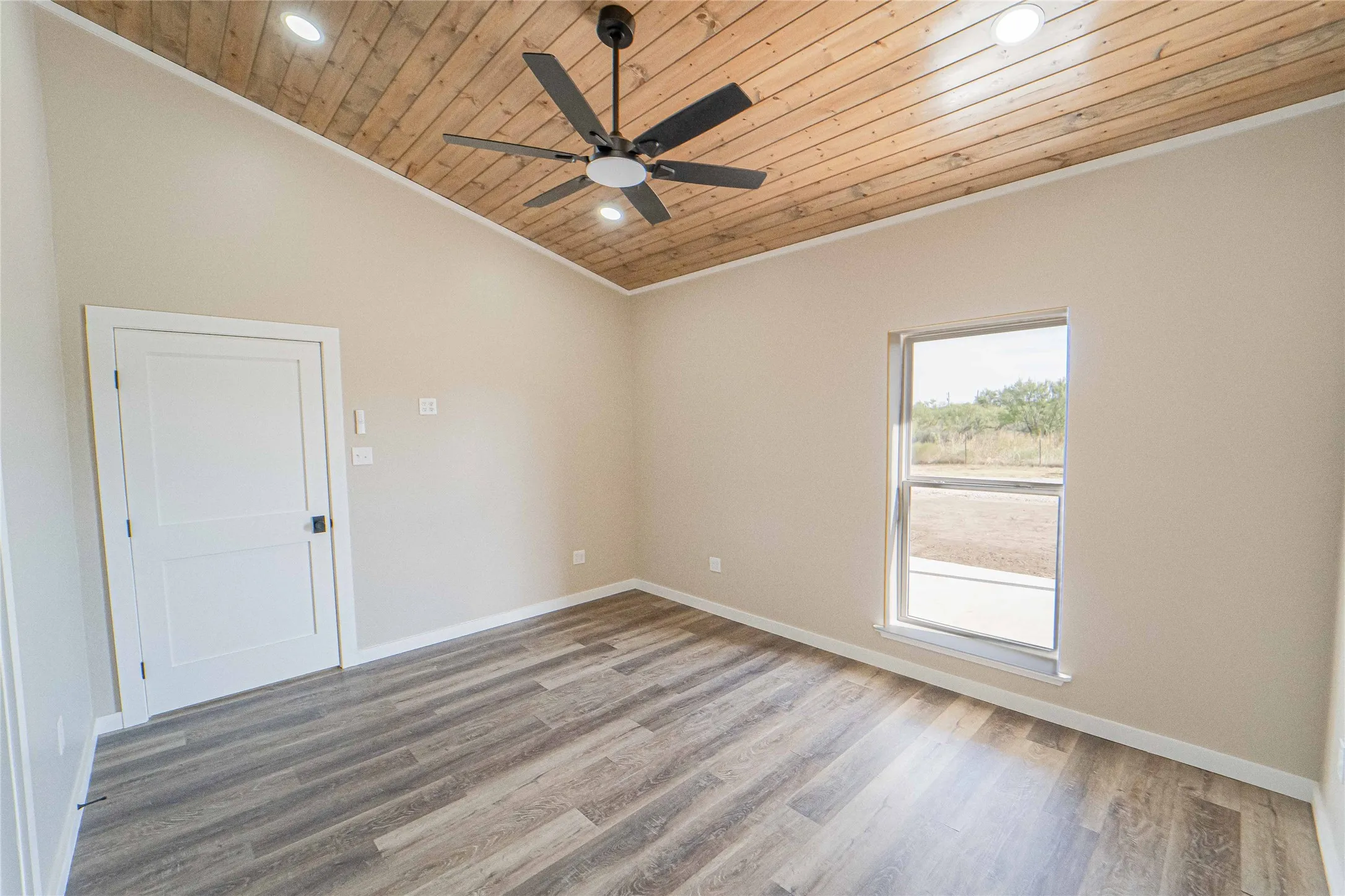 Primary room with vaulted wood-finish ceiling, wood-finish flooring, single window, white paneled door, and ceiling fan with integrated lighting