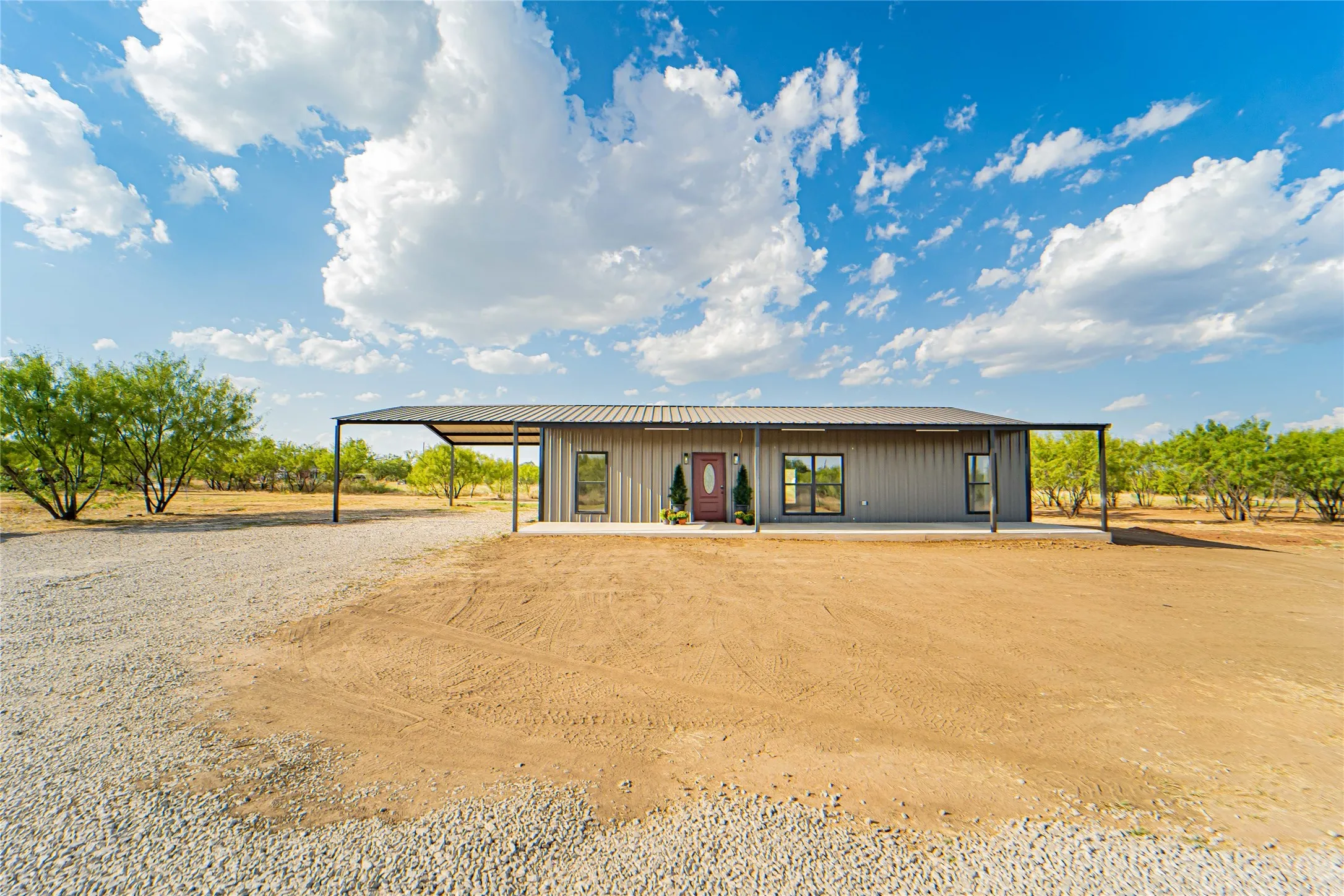 Metal-sided exterior with a dark metal roof, featuring a red entry door and an expansive gravel driveway