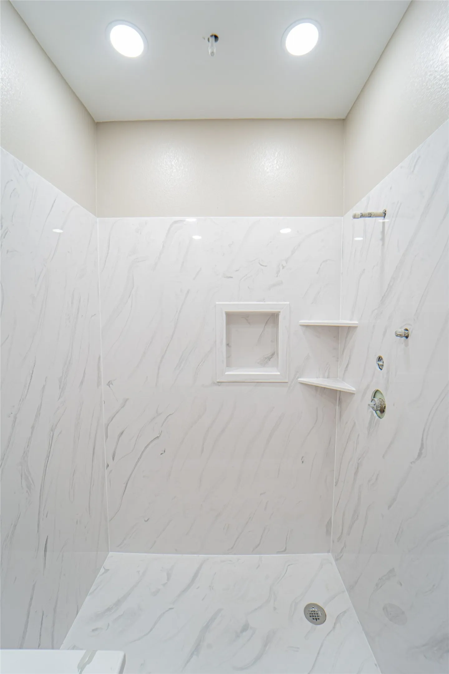 Tiled shower enclosure featuring a built-in niche, two recessed lights, and a chrome shower fixture