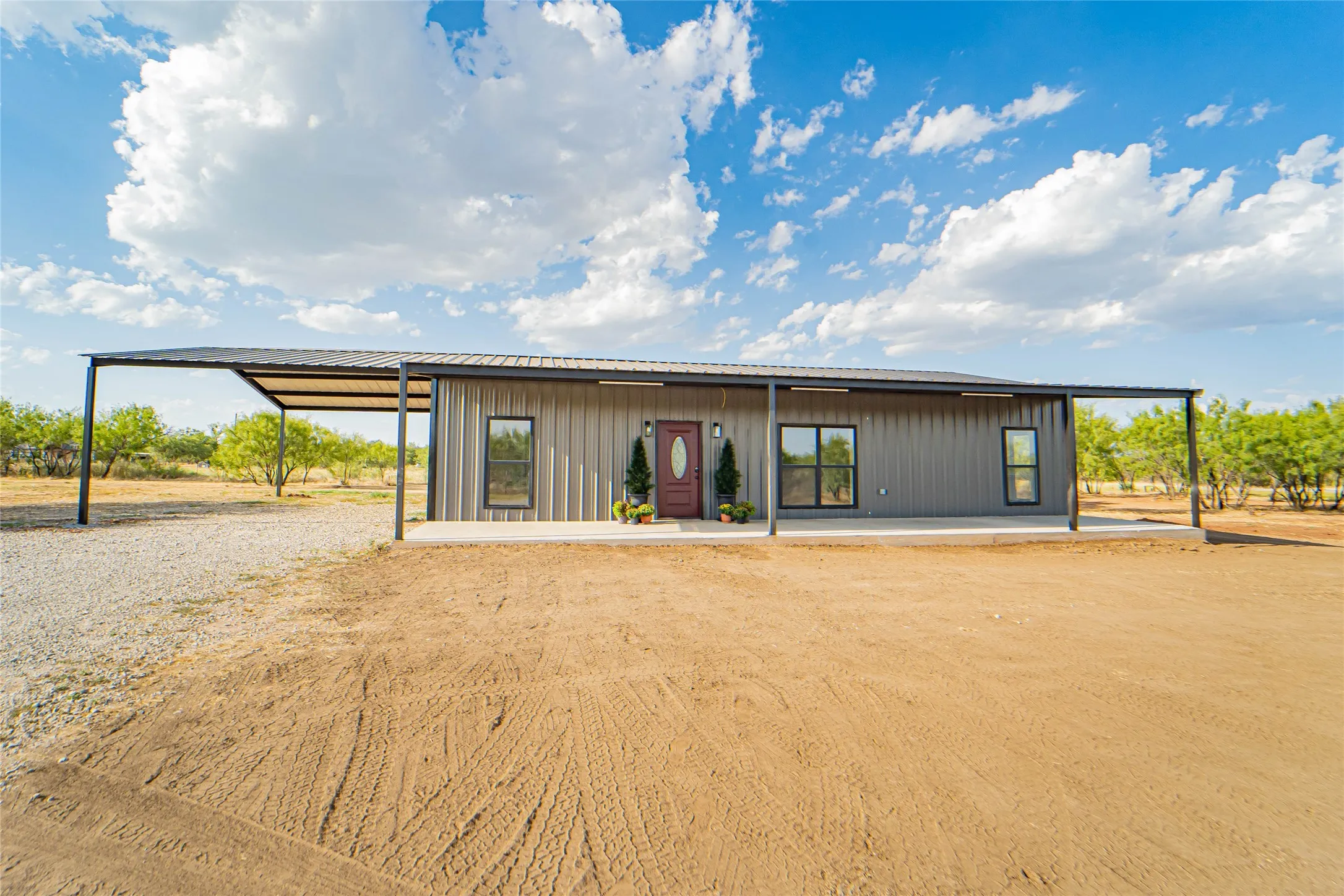 Metal siding residence featuring a covered front porch, dark-framed windows, and a detached carport