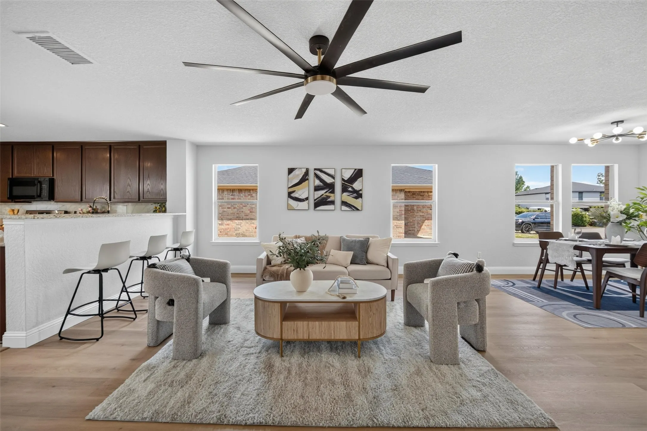 Open-concept living space featuring wood-finish flooring, a contemporary ceiling fan, and multiple windows