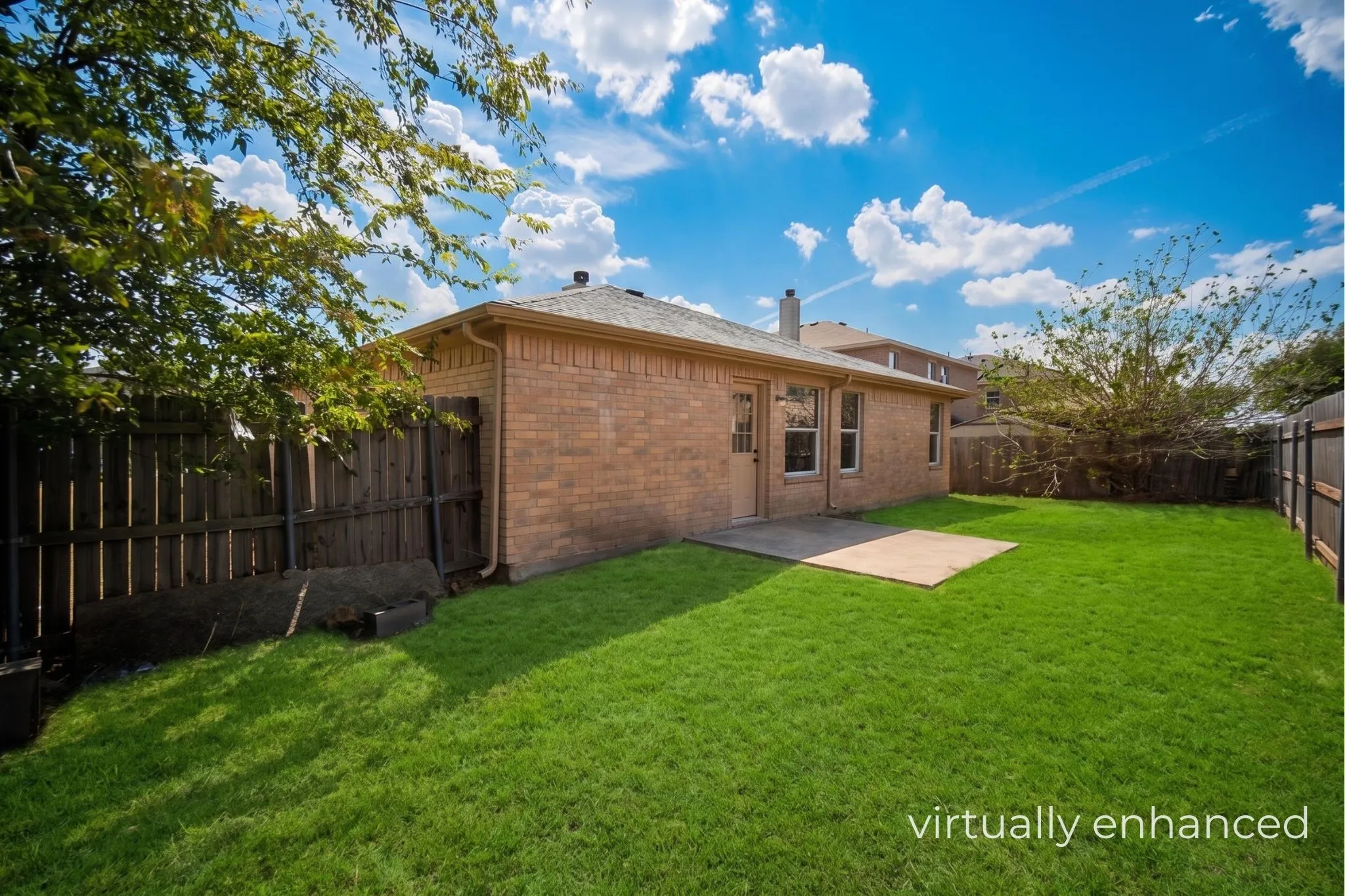 Expansive green lawn with a brown brick exterior, privacy fencing, and a concrete patio