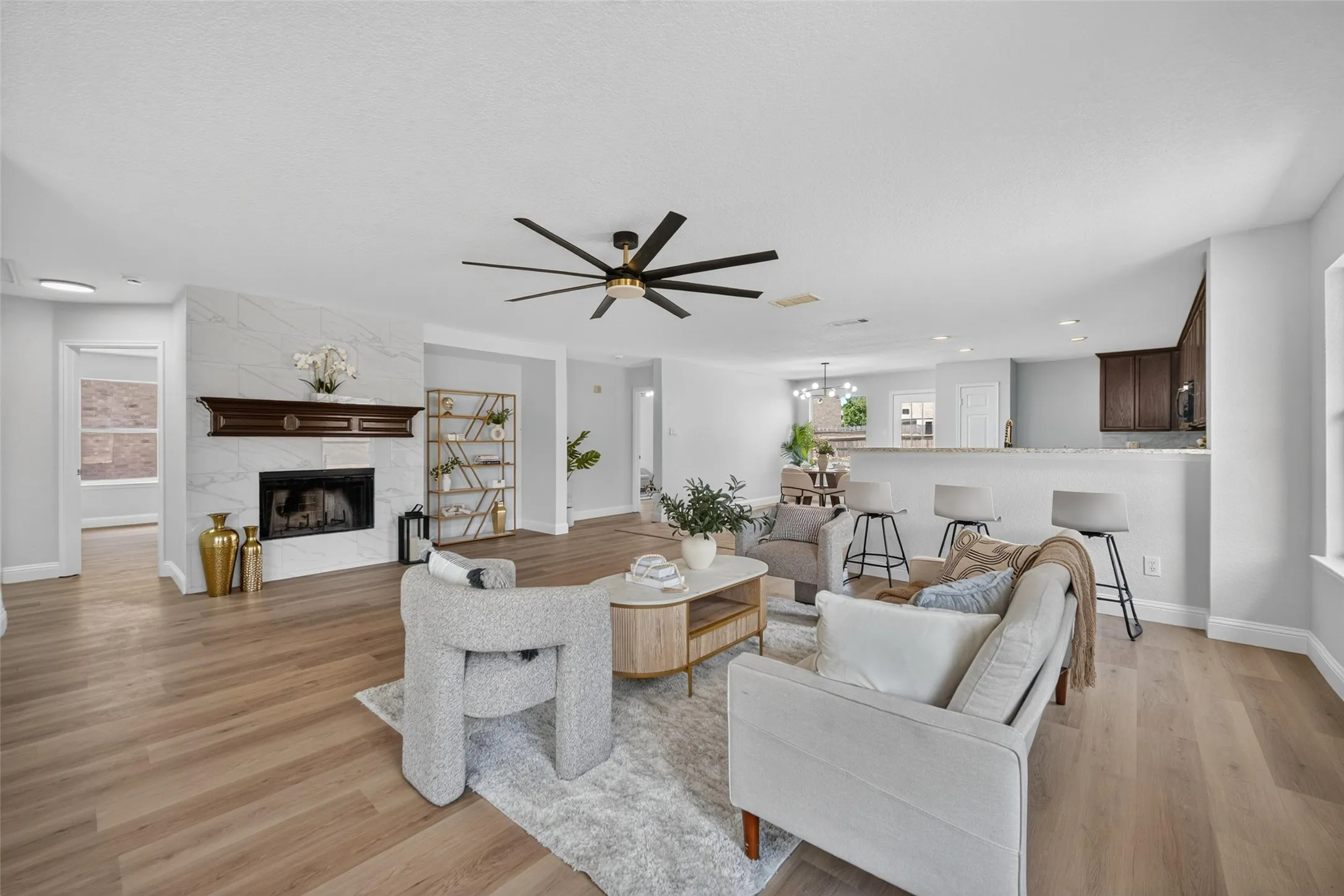 Open-concept living area featuring wood-finish flooring, a contemporary ceiling fan, and a fireplace with a white tile surround and dark wood mantel