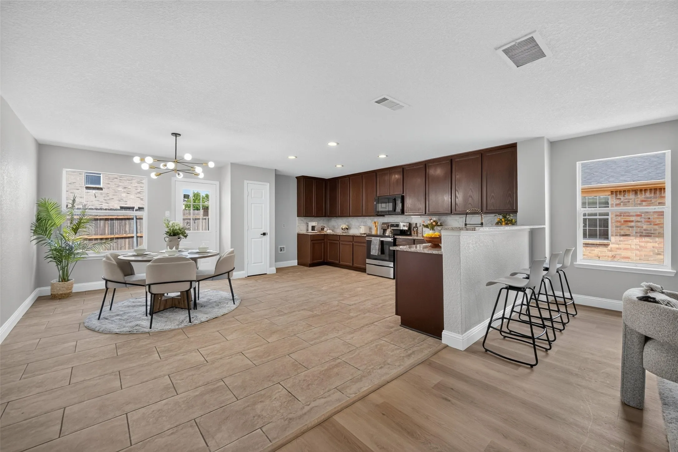 Spacious open-concept living area featuring wood-finish flooring, ample natural light, and a modern kitchen with dark wood cabinetry