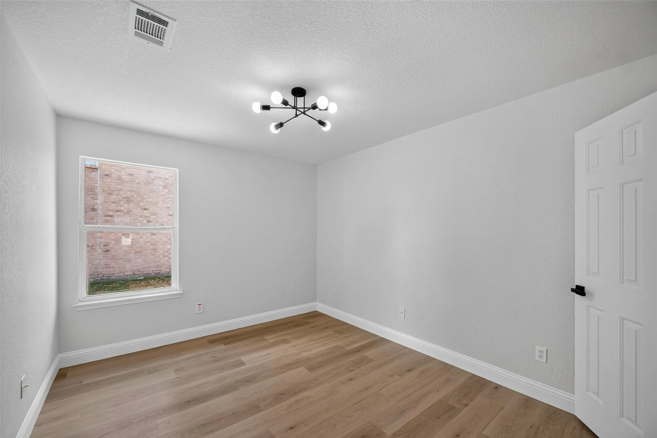 Wood-finish flooring, white trim, modern sputnik light fixture, paneled door with black hardware, and a double-hung window