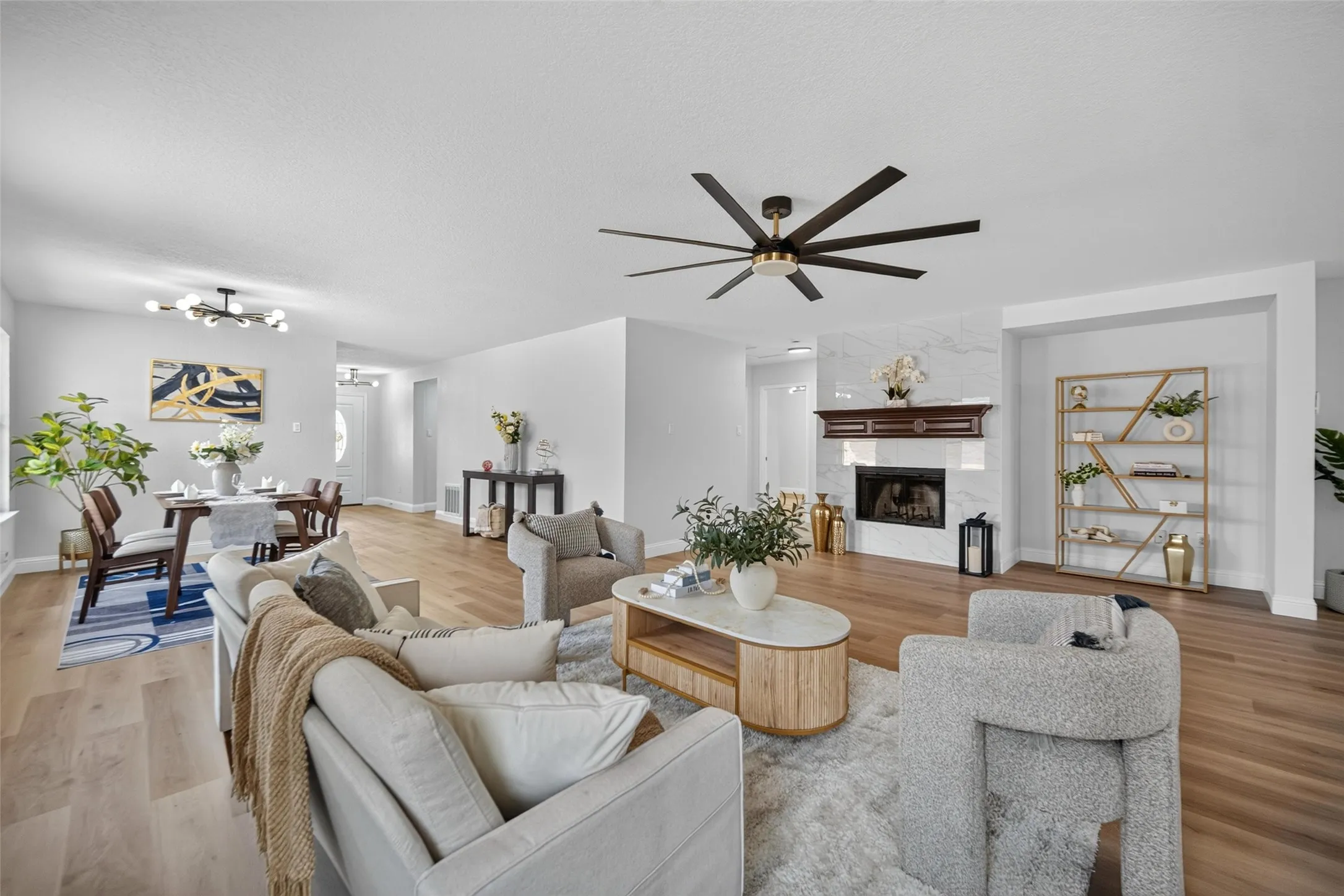 Open-concept living area with wood-finish flooring, a contemporary ceiling fan, and a fireplace featuring a marble-look surround and a dark wood mantel