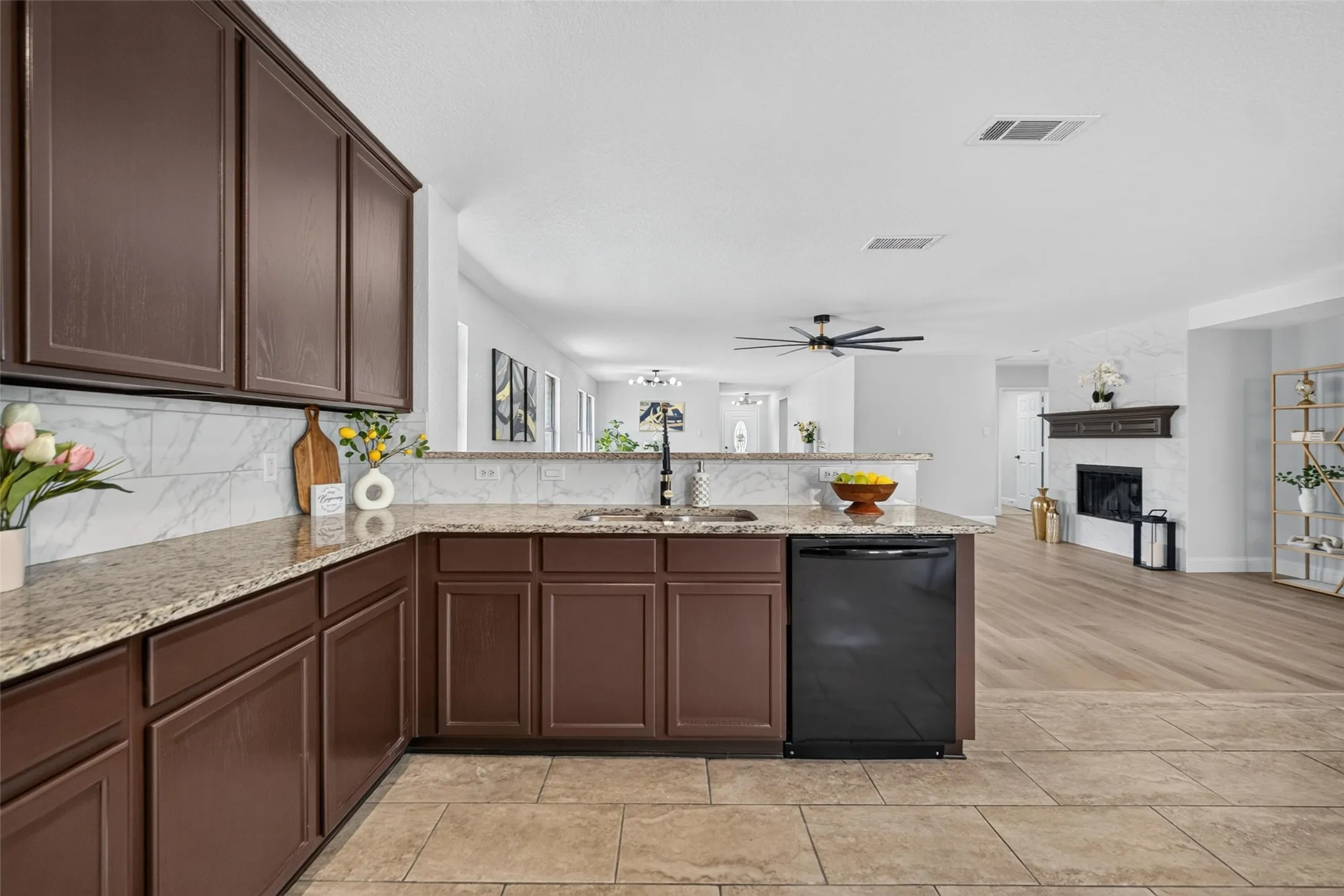 Kitchen featuring dark wood cabinetry, light granite countertops, a built-in dishwasher, and a white tile backsplash