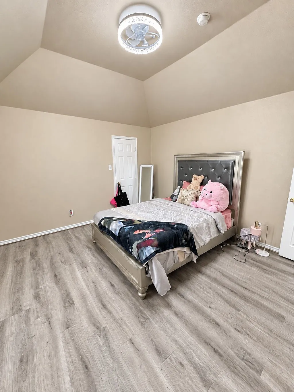 Vaulted ceiling, modern flush-mount ceiling light with fan, light wood-finish flooring, and painted walls
