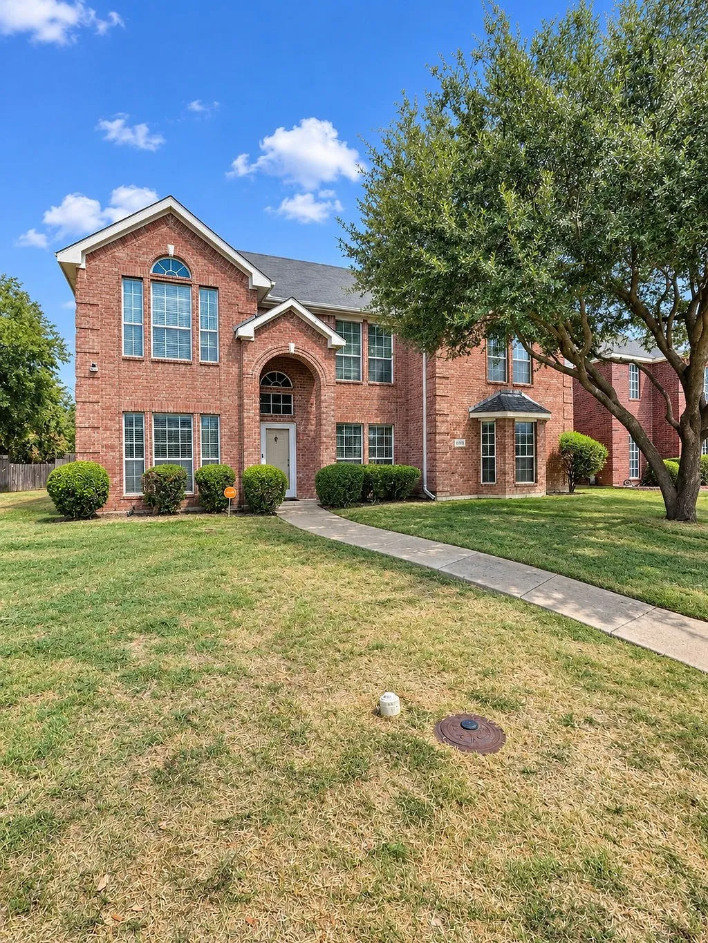 Red brick exterior with multiple window styles, arched entry, and a mature tree