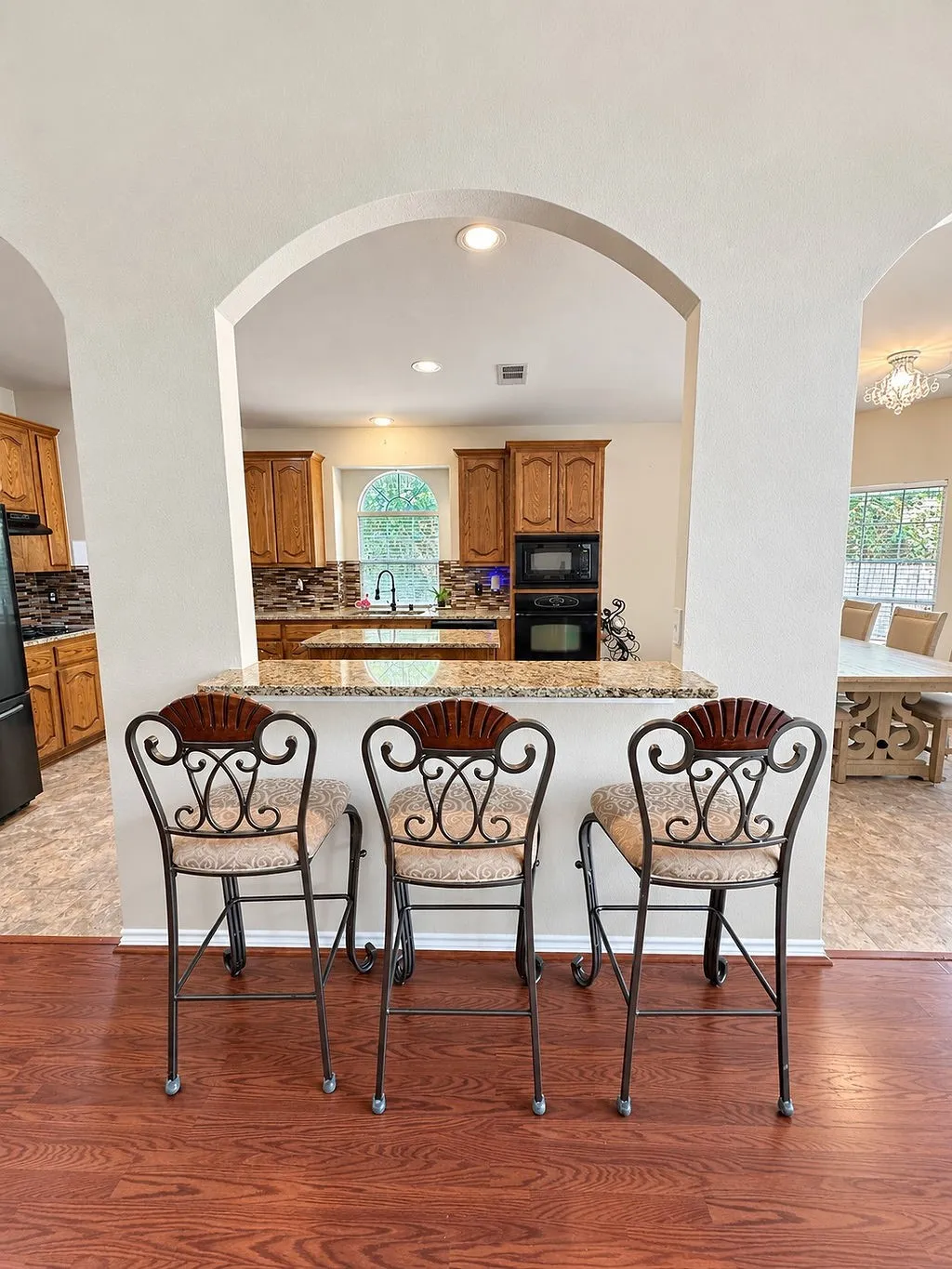 Archway opening to a kitchen featuring warm wood cabinetry, built-in appliances, and a tiled backsplash