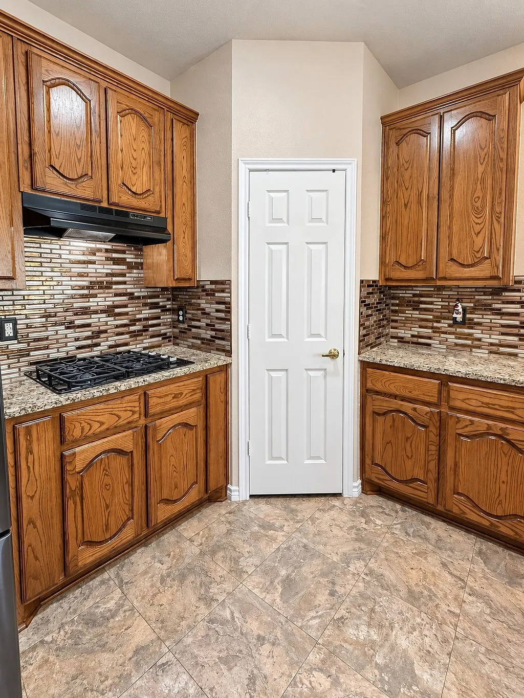 Kitchen featuring wood cabinetry, granite-style countertops, mosaic tile backsplash, and a gas cooktop with an integrated vent hood