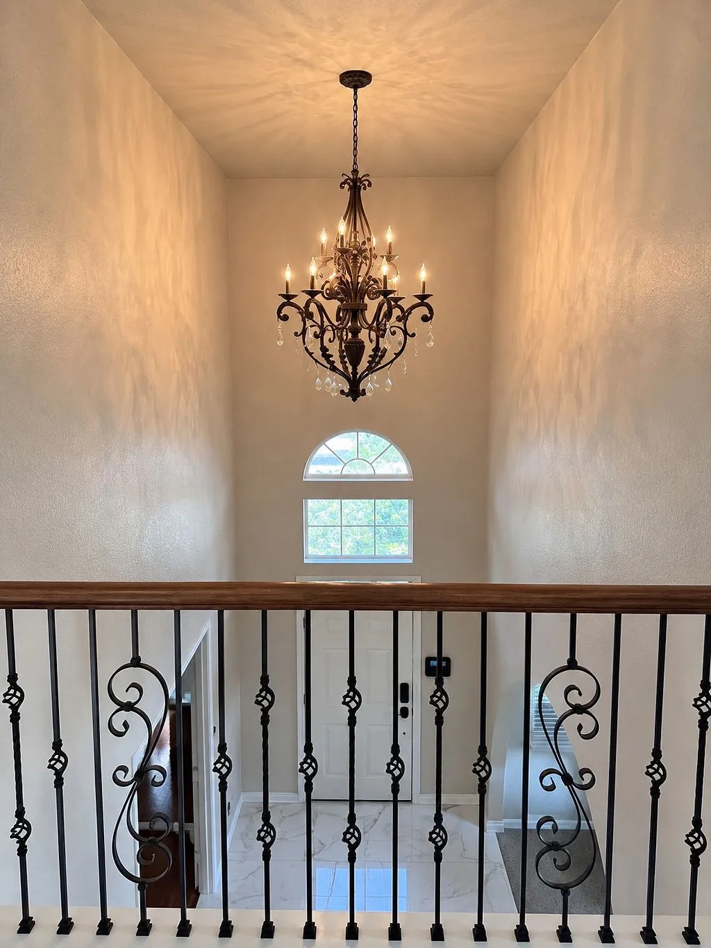 Two-story entry featuring an ornate chandelier, arched window, and wrought iron balusters with wood-finish railing