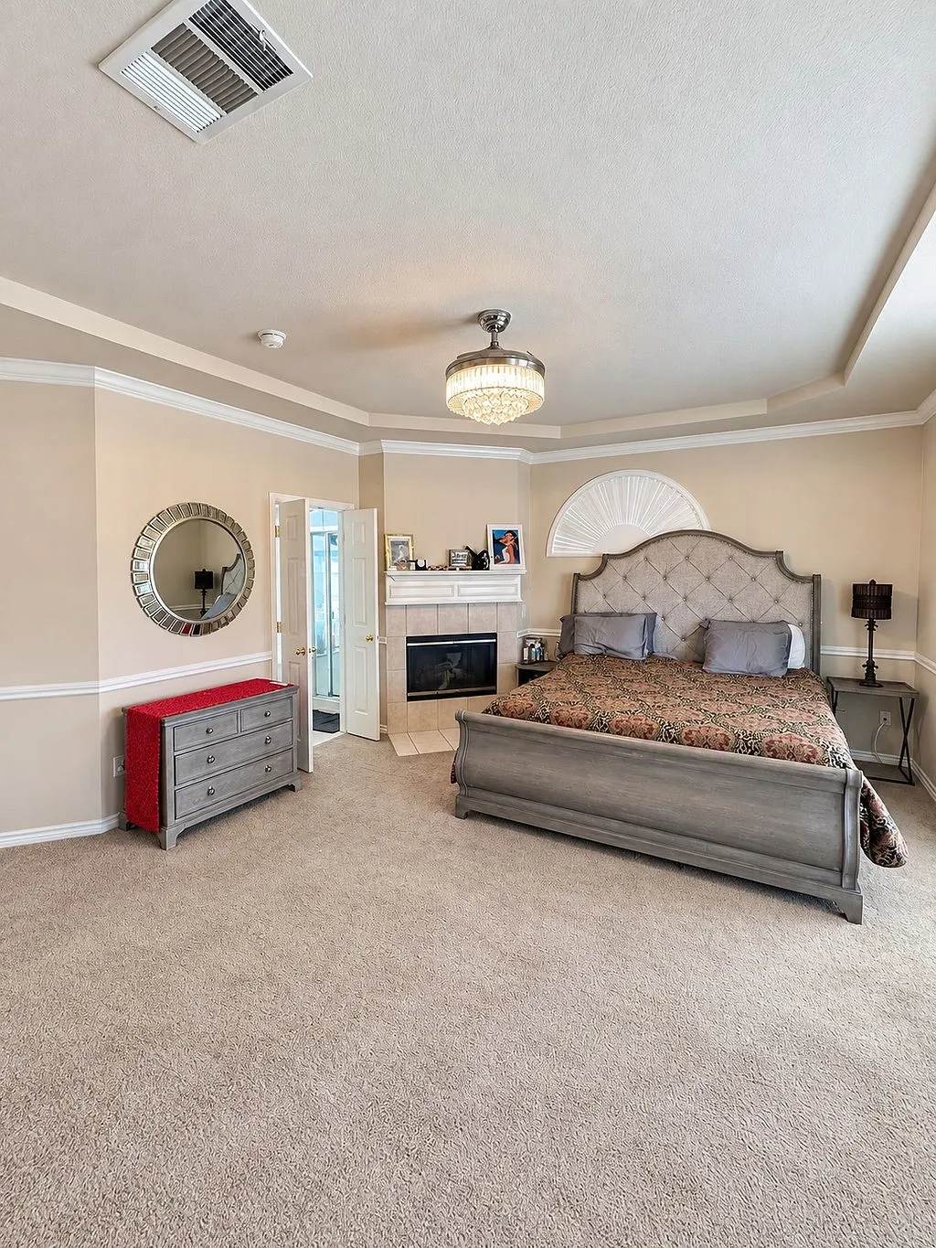 Recessed tray ceiling with crown molding, decorative chandelier, and an integrated fireplace with a tile surround