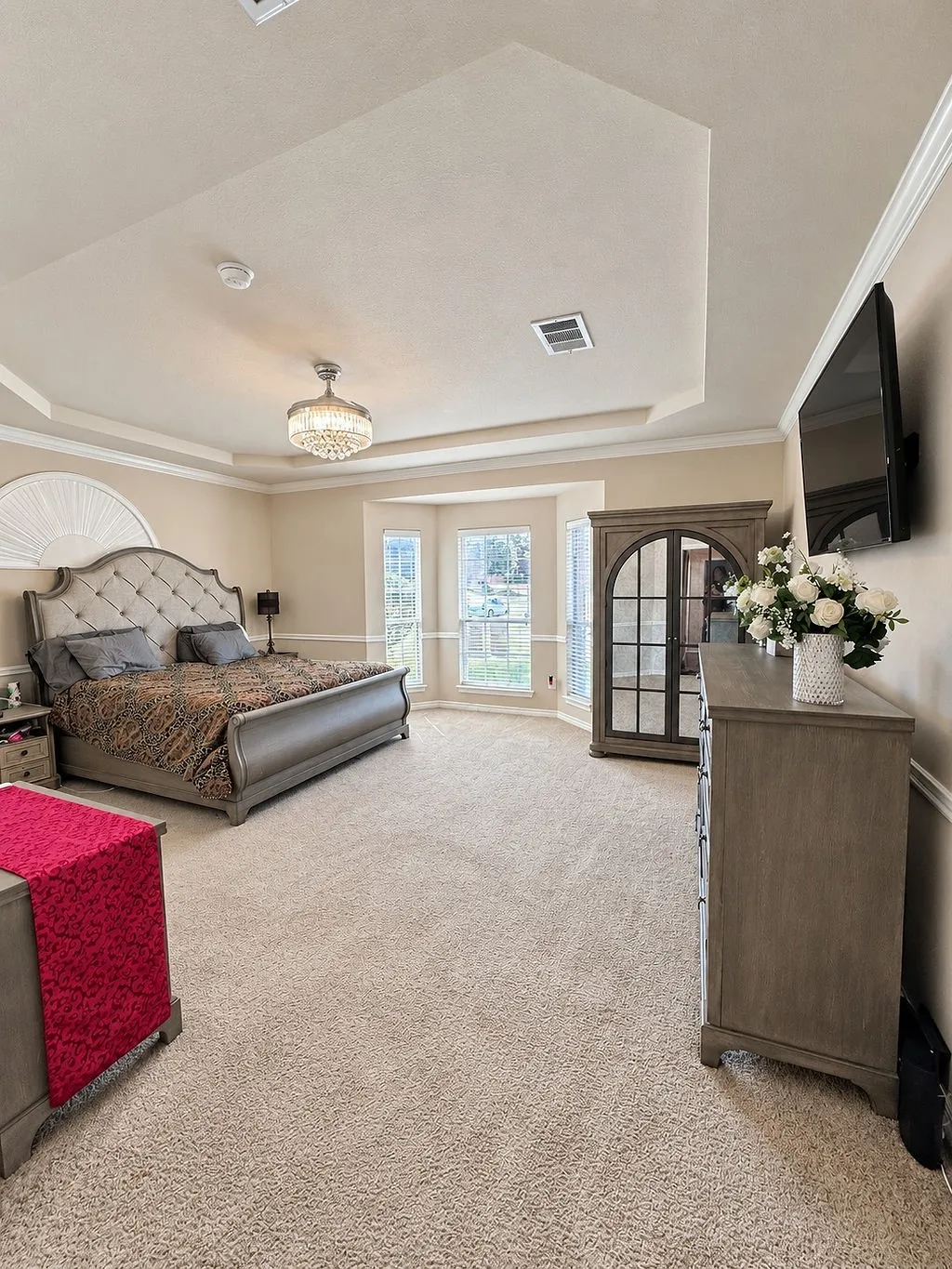 Tray ceiling with crown molding, chandelier, bay windows, and neutral carpeting