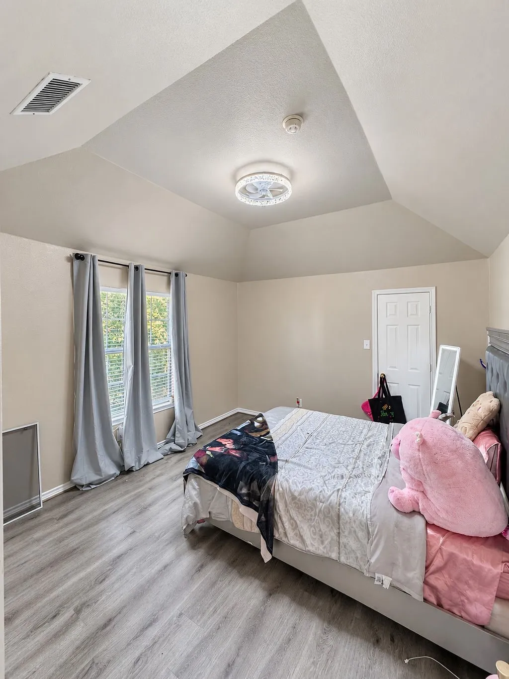 Vaulted ceiling with an attached ceiling light fixture, wood-finish flooring, and two windows with blinds