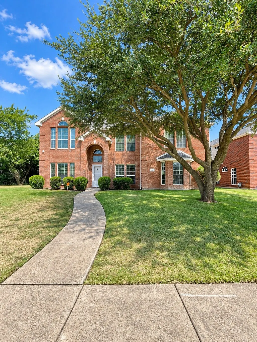 Traditional brick exterior with arched entry, bay window, and a mature shade tree