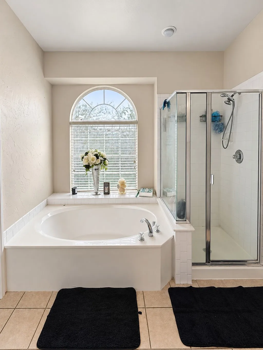 Built-in soaking tub with a tiled surround, arched window, and adjacent glass-enclosed shower