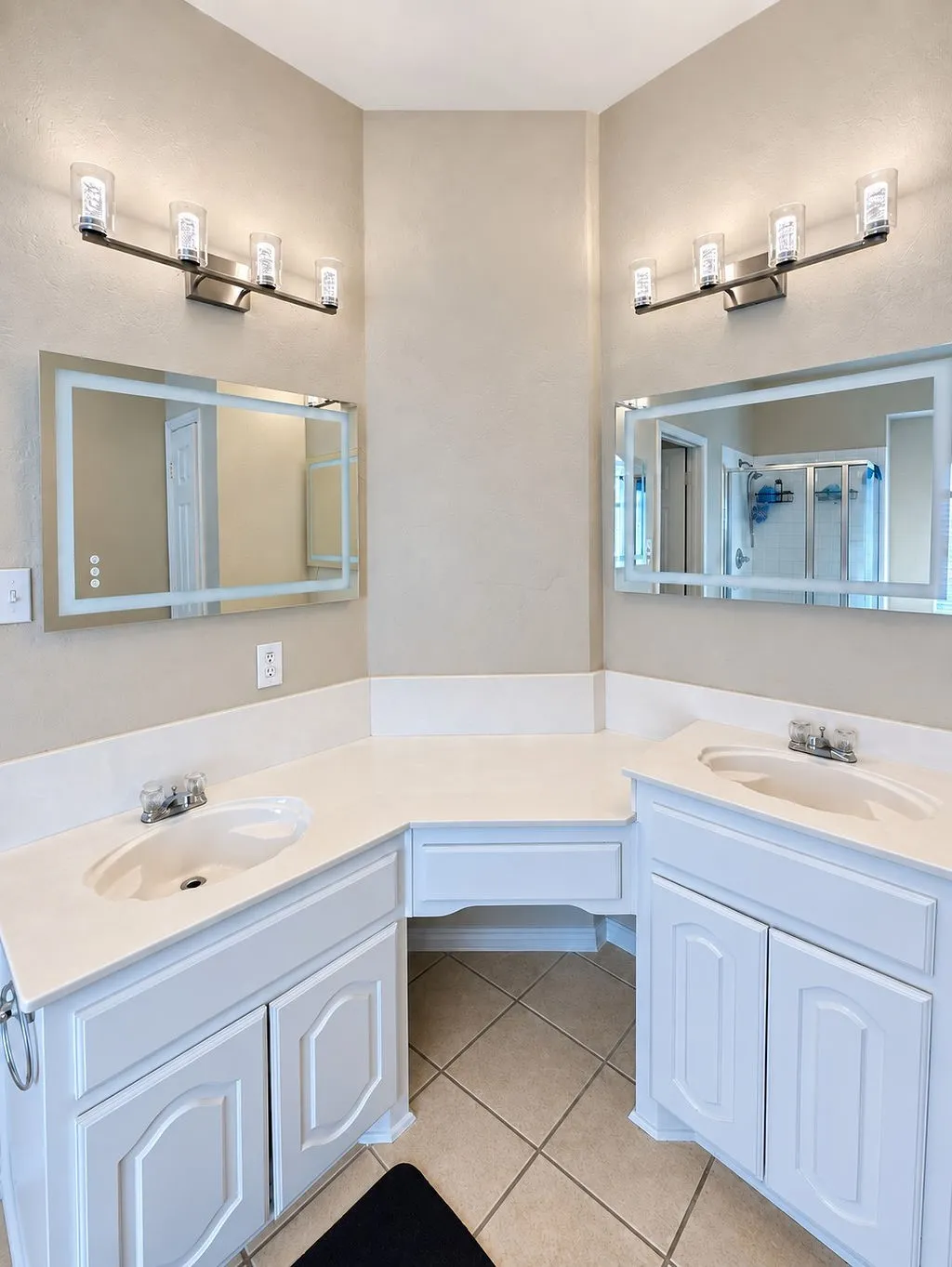 Dual vanity sinks with white cabinetry, integrated makeup vanity, tile flooring, and contemporary wall sconces