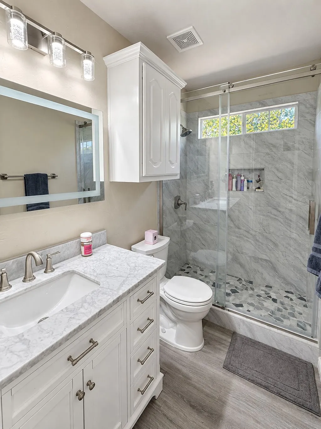Tiled walk-in shower with a glass enclosure, wood-finish flooring, white vanity with a light-colored countertop, and a mirrored medicine cabinet