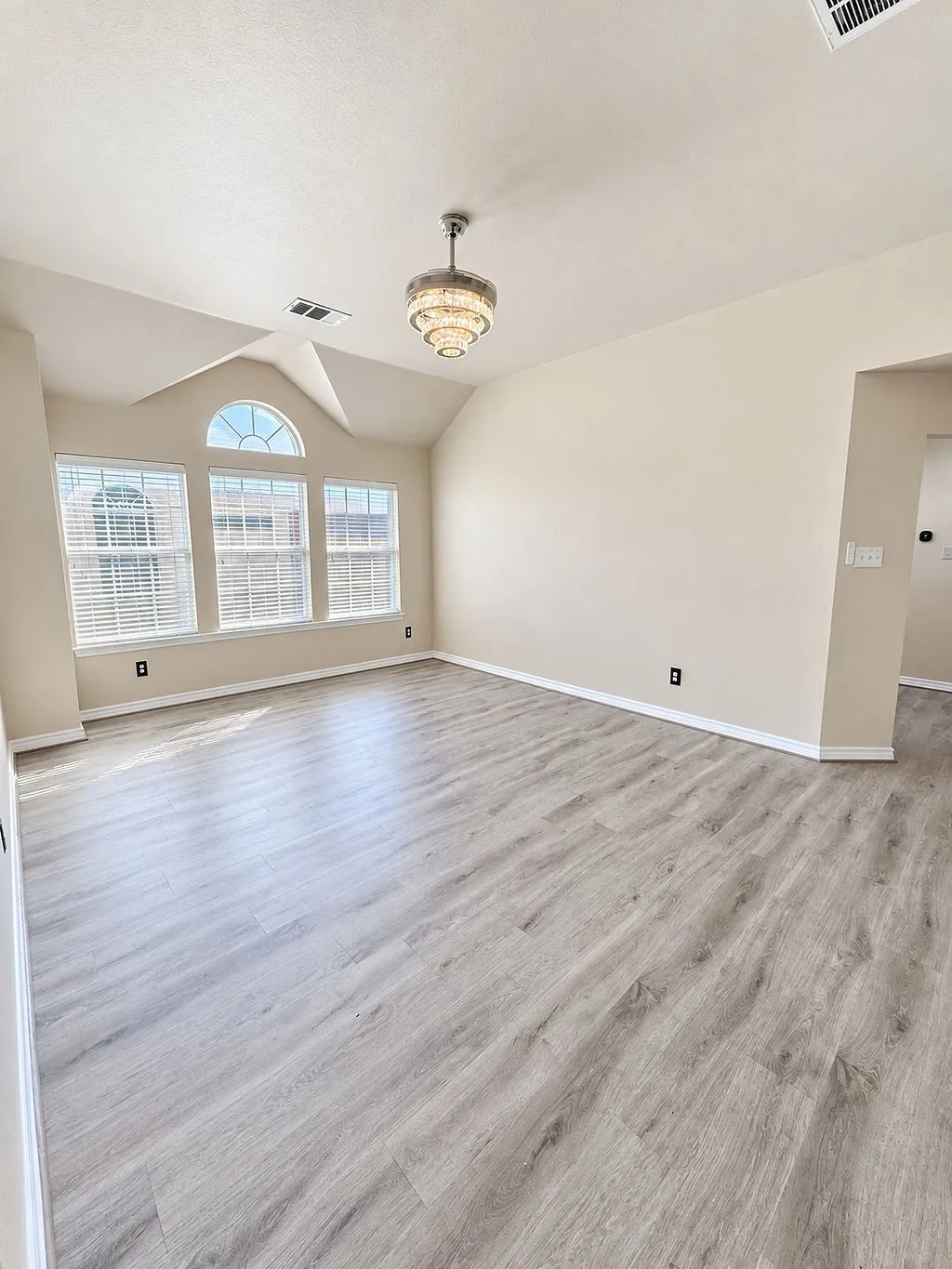 Vaulted ceiling with an ornate chandelier, multiple windows, arched transom window, and wood-finish flooring