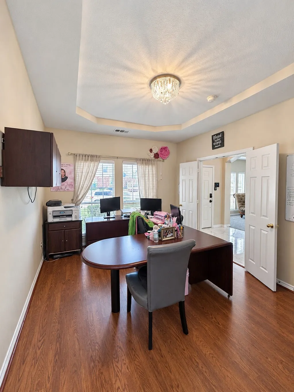 Wood-finish flooring throughout, tray ceiling with crystal chandelier, and paneled double doors
