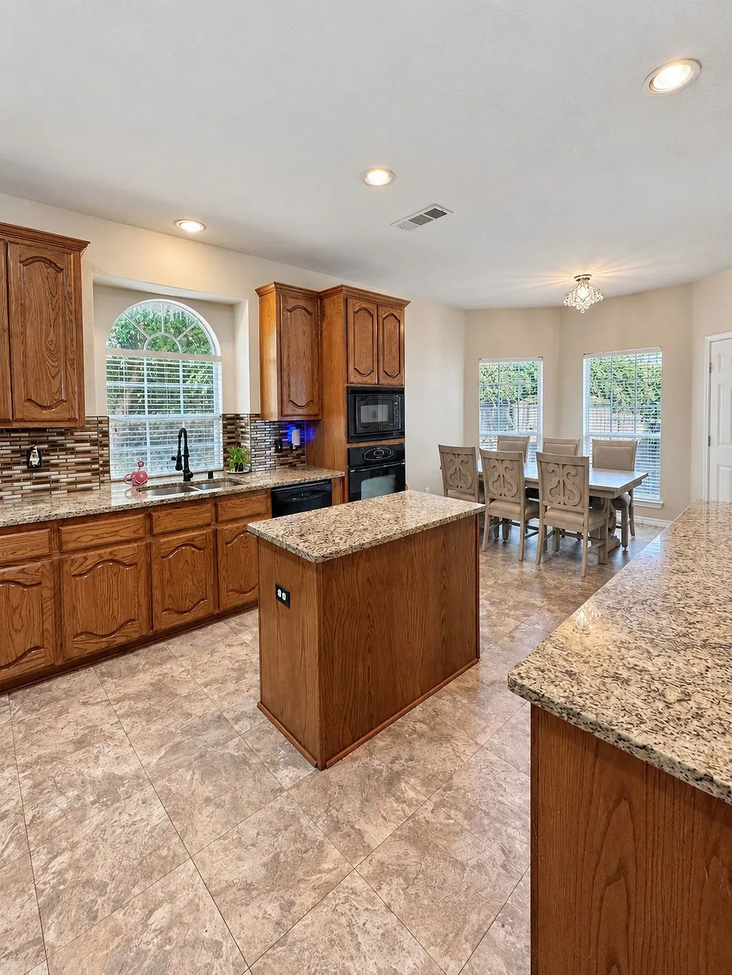 Kitchen featuring a central island, granite countertops, wood cabinetry, tile flooring, and recessed lighting