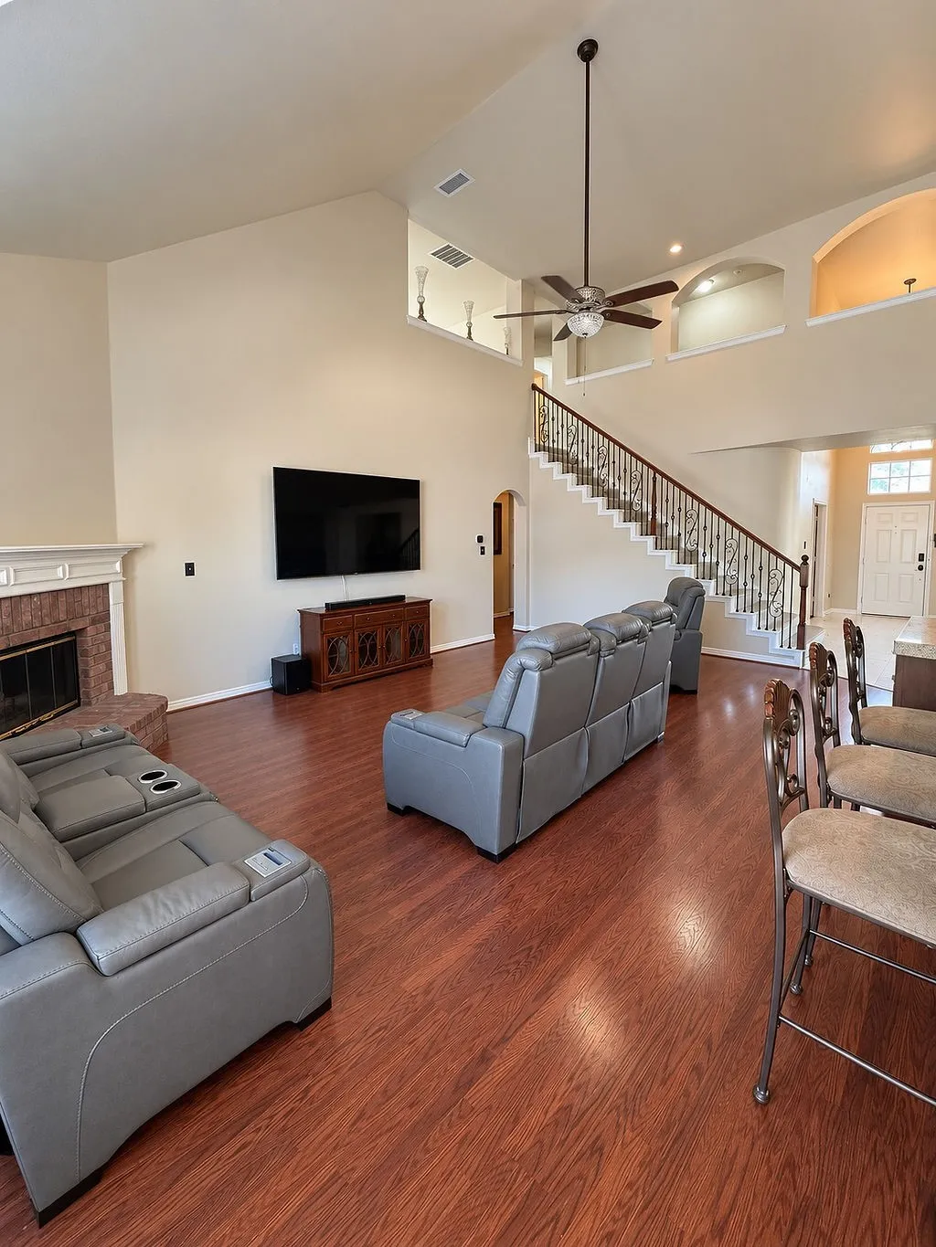 Vaulted ceiling with a ceiling fan, fireplace with a mantel, wood-finish flooring, staircase with metal balusters, and arched wall niches