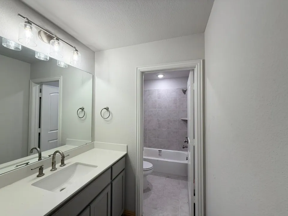 Vanity with an integrated sink and brushed nickel faucet, a large mirror, and a four-light fixture