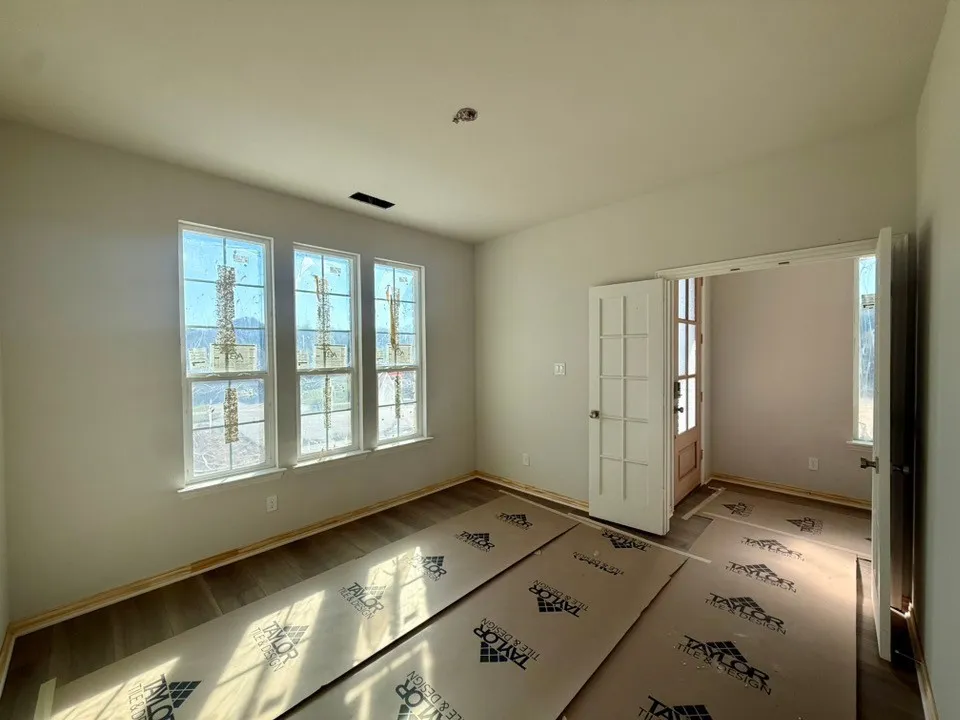 Three large windows, wood-finish flooring, and a paneled interior door with frosted glass inserts