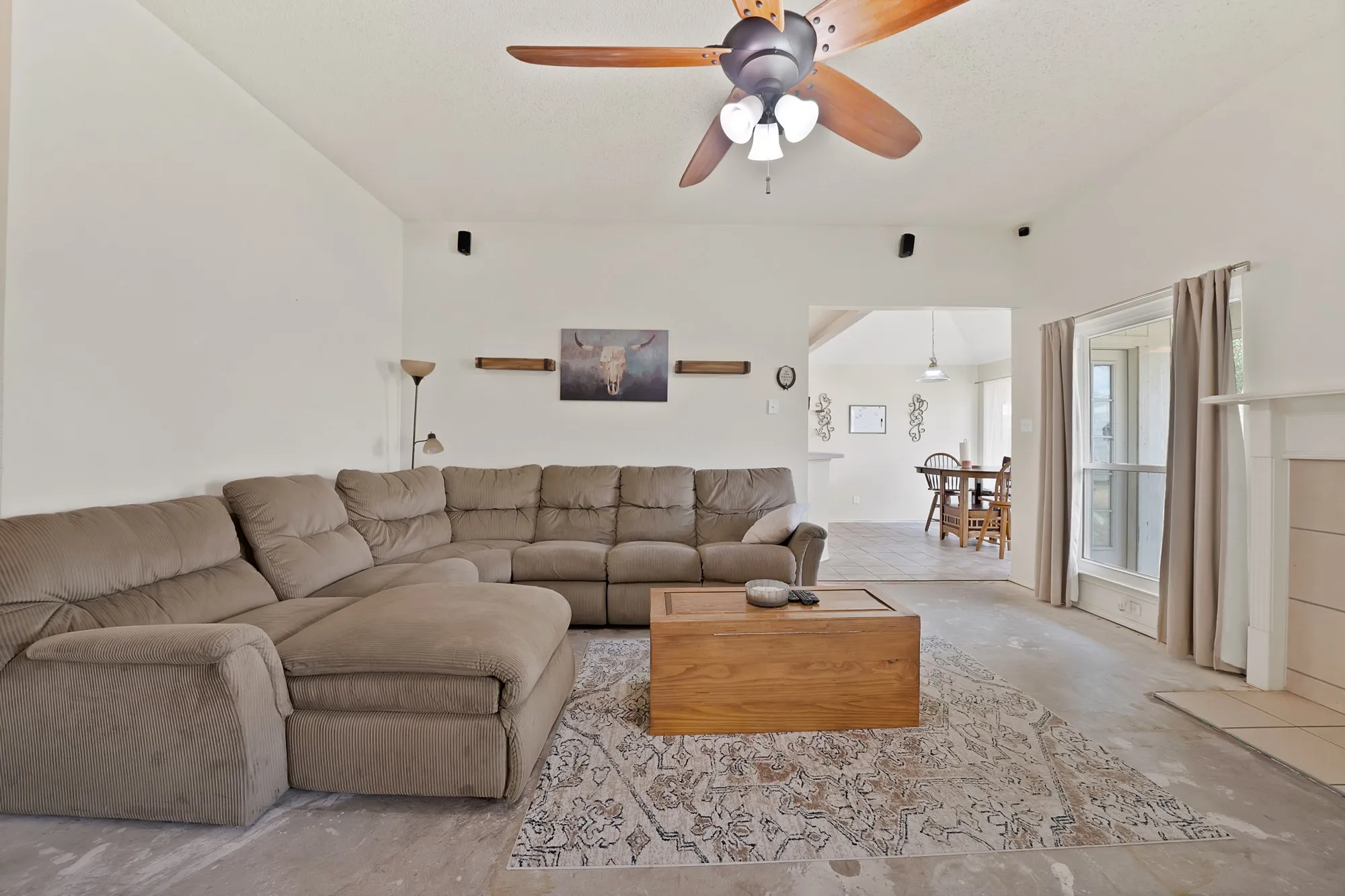 Vaulted ceiling with a ceiling fan, bay window, and a fireplace with a mantel