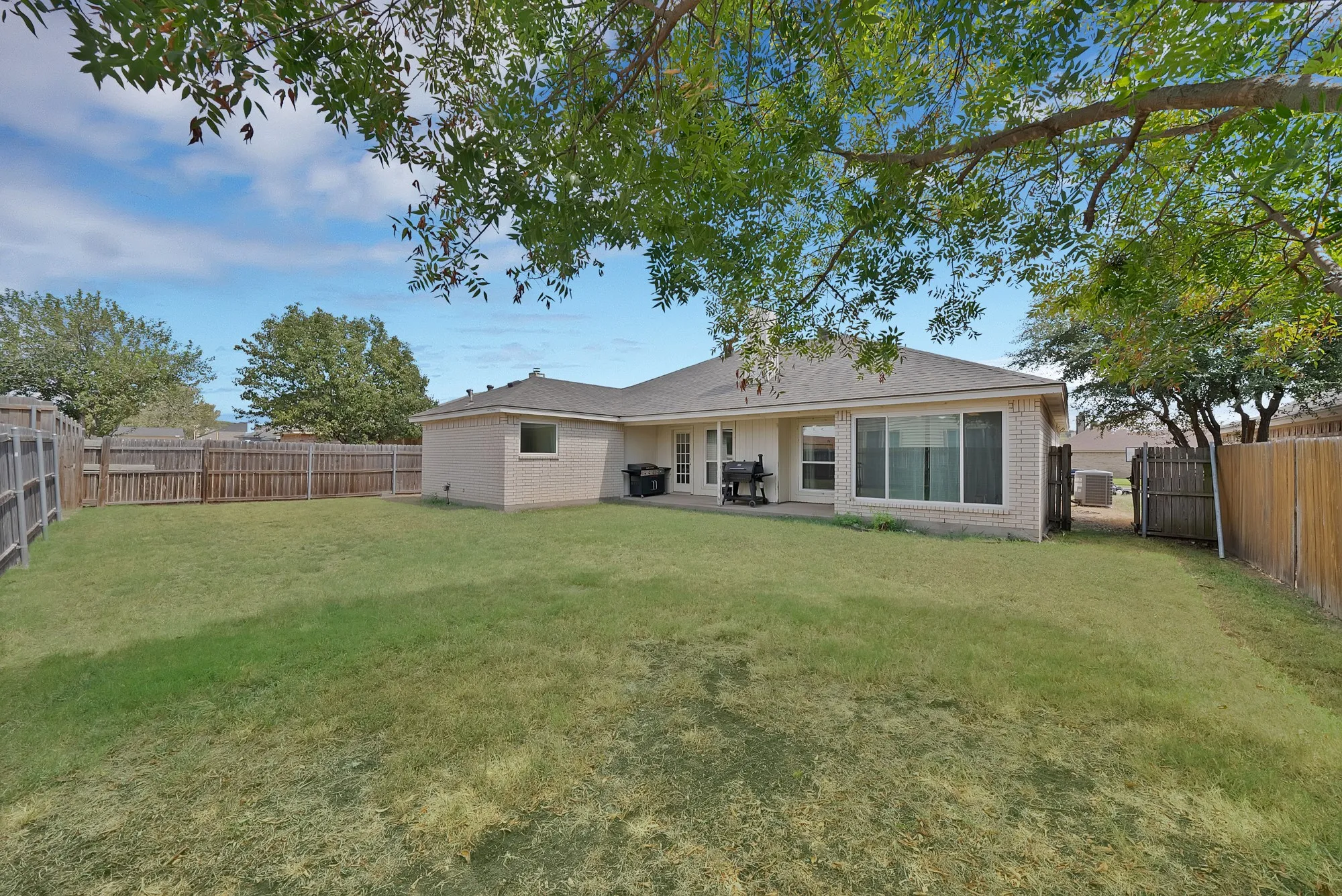 Expansive backyard with a manicured lawn, full perimeter wood fencing, and a brick-clad exterior