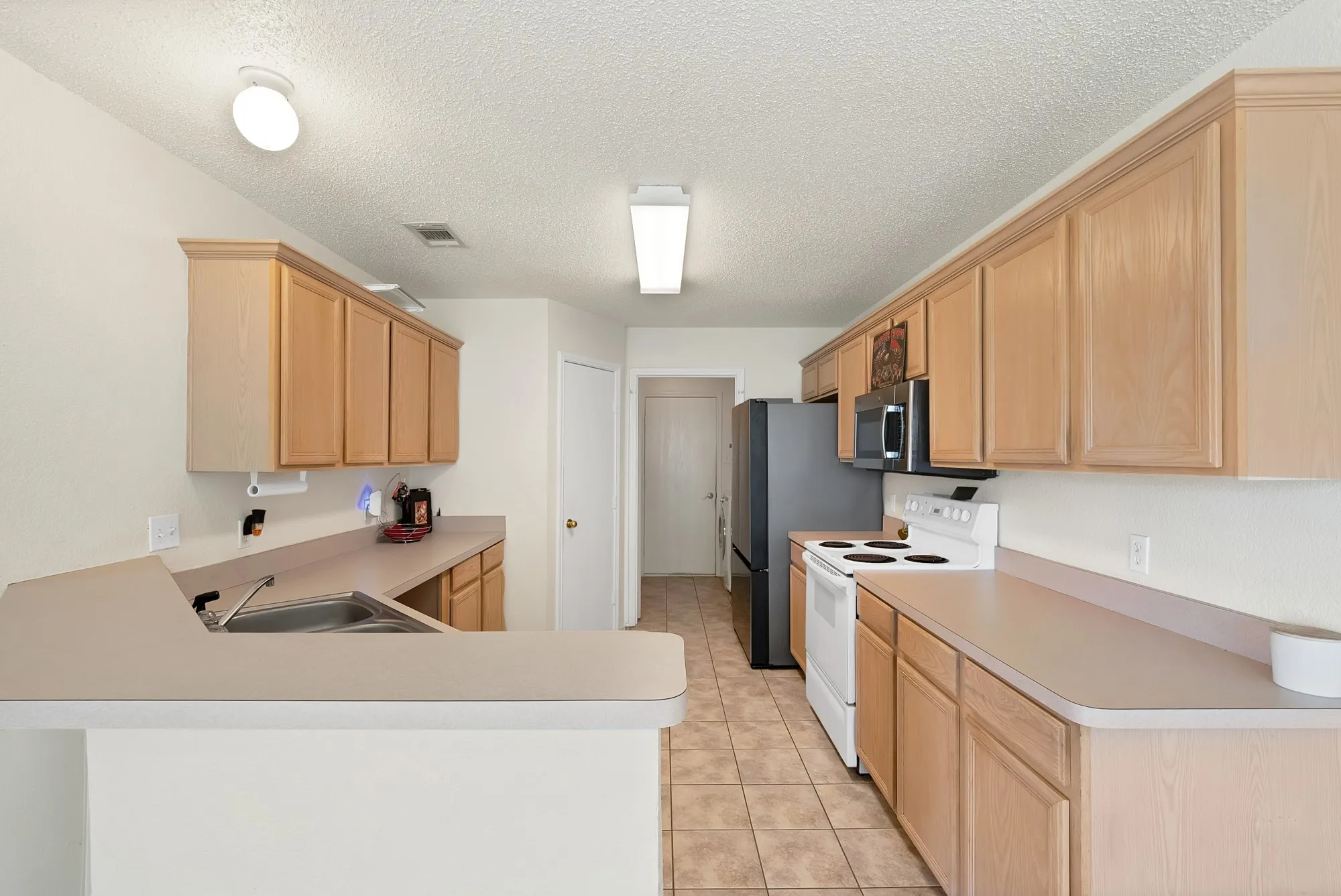 Light-toned wood cabinetry with crown molding, solid surface countertops, stainless steel sink, tiled flooring, and a full suite of appliances