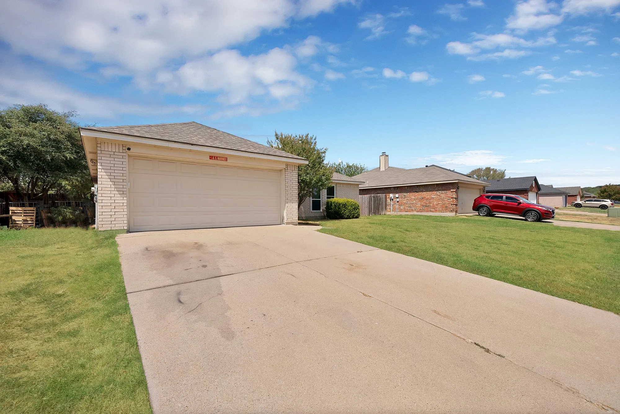 Attached garage with a light-colored door, brick facade, and a concrete driveway