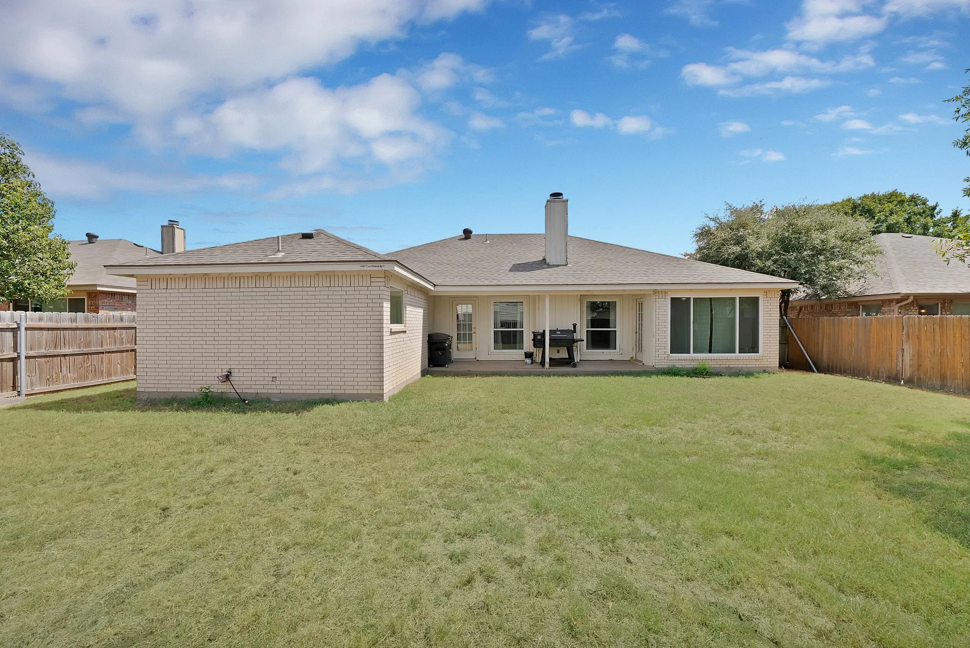 Expansive backyard featuring a manicured lawn, brick exterior, full privacy fencing, and a concrete patio