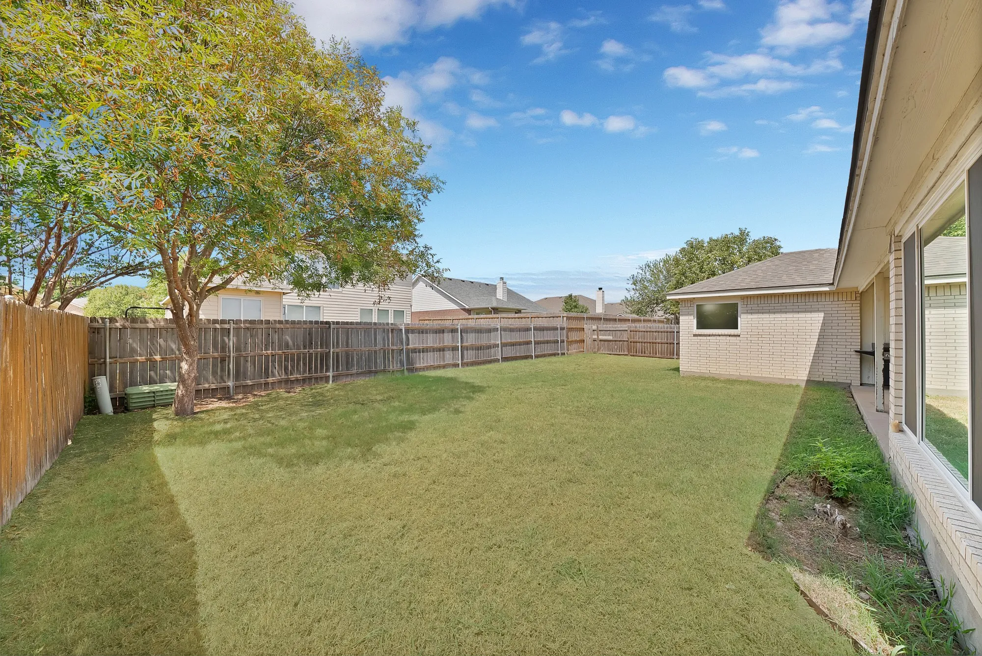 Expansive grassy yard with mature tree and wood privacy fence
