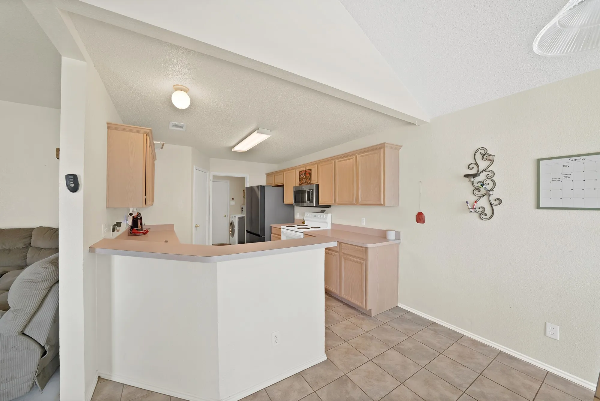 Kitchen featuring wood cabinetry, tiled flooring, a serving counter, and vaulted ceilings