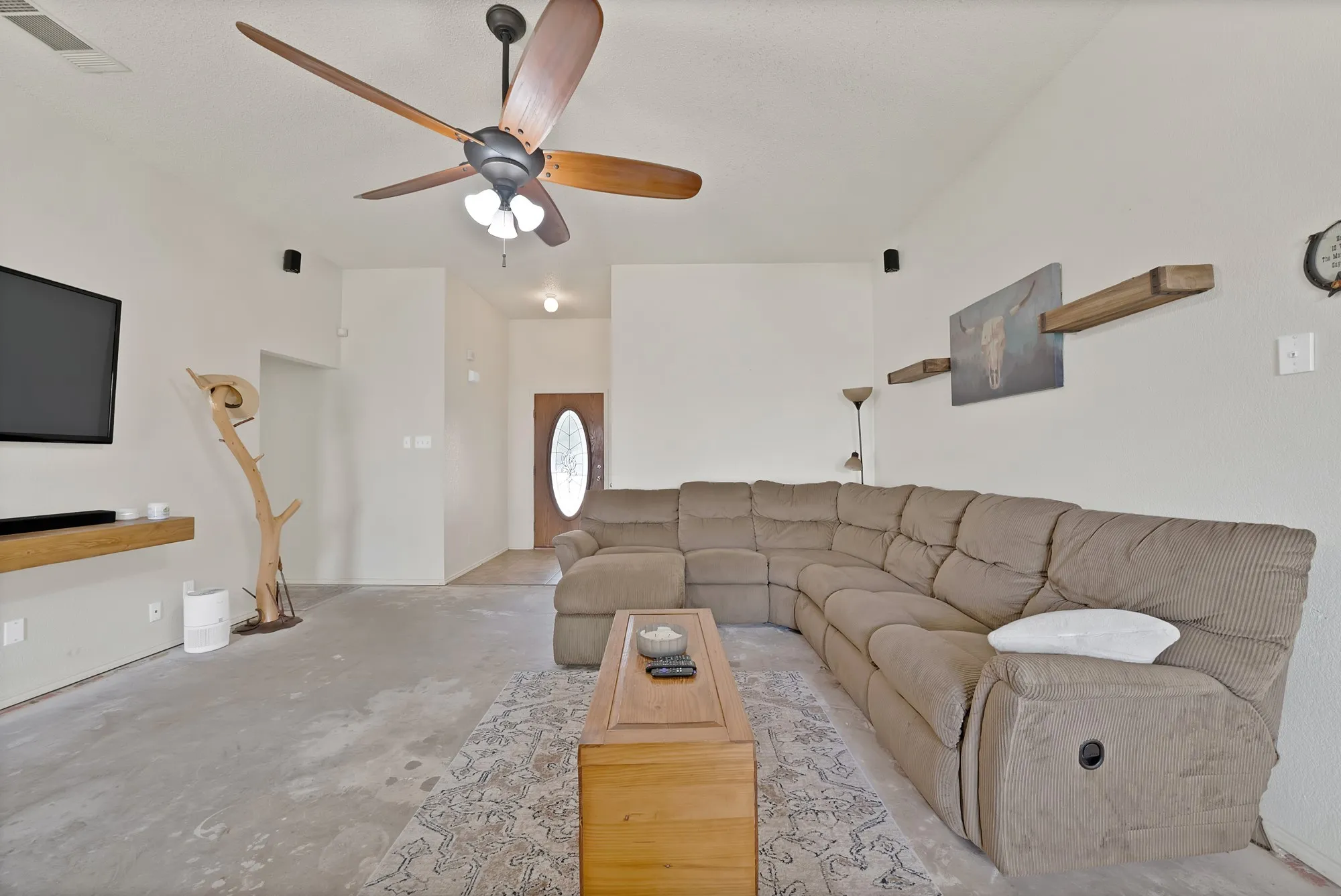 Vaulted ceiling with a ceiling fan, wall-mounted display shelves, and a front entry door with an oval glass insert